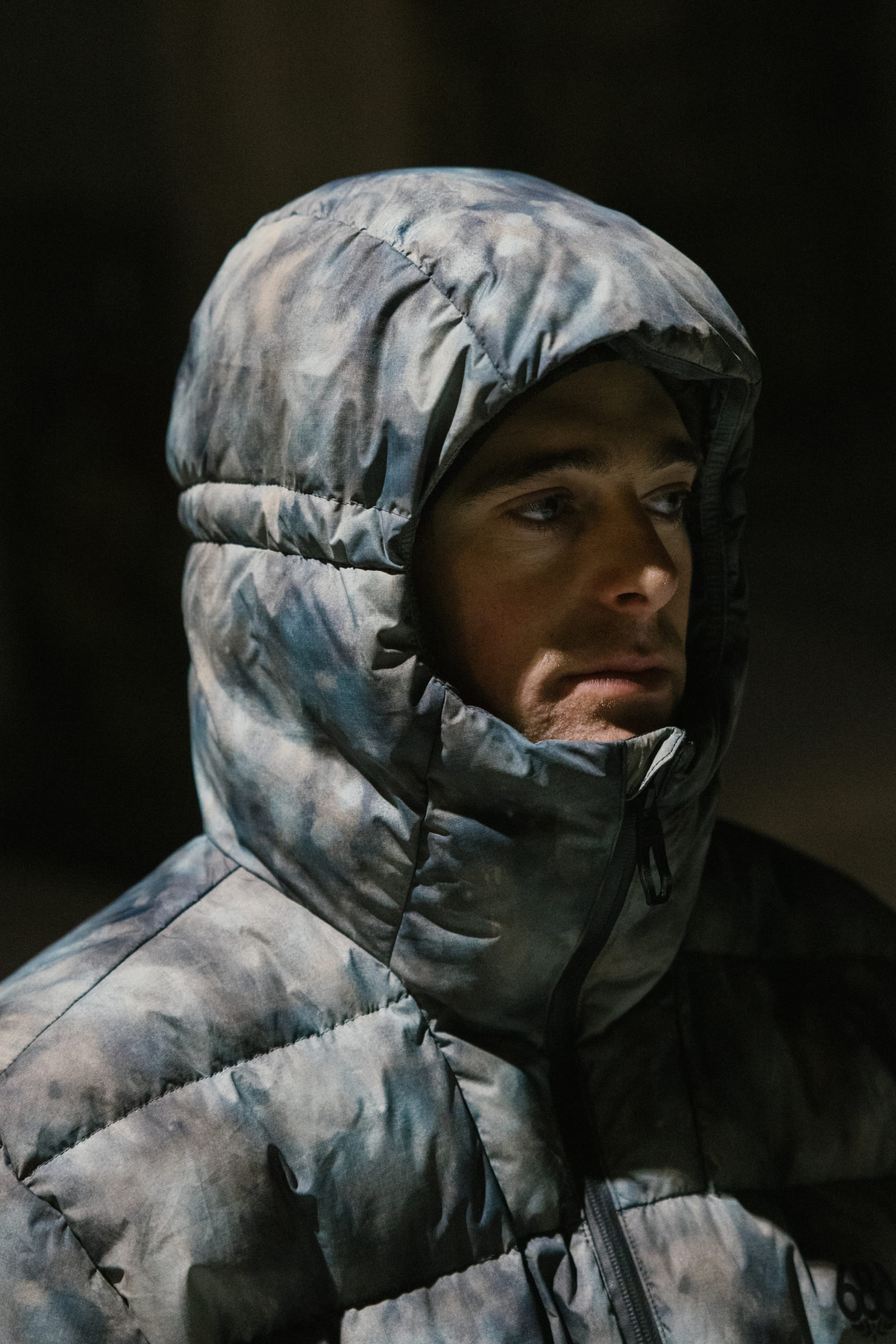 A person wearing the 686 Men’s WINDSTOPPER® Pyro™ Down Puffer Jacket by GORE-TEX® LABS with the hood up, looking to the side in low light.