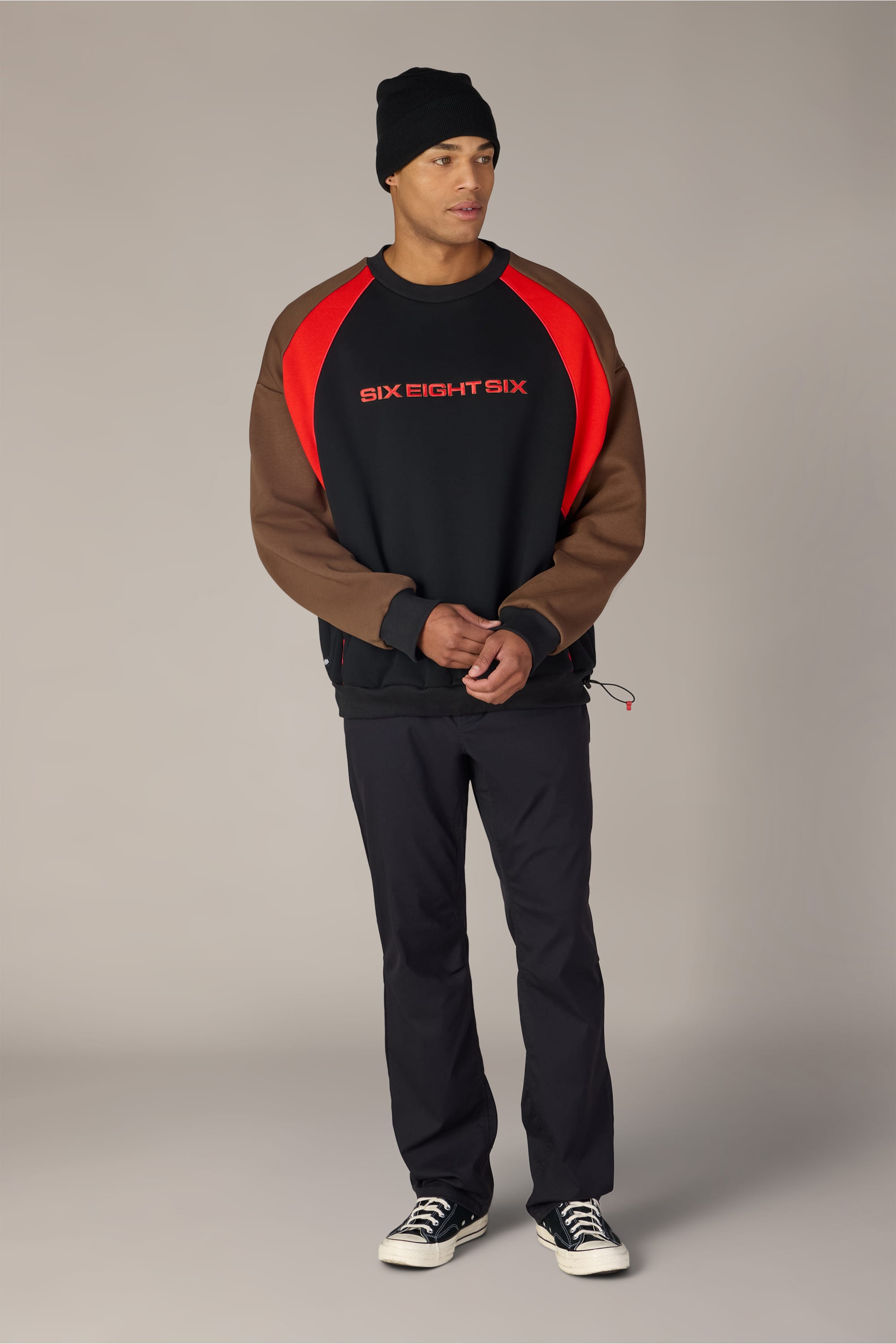 A person wearing a black beanie and the 686 Reserved® Premium Heavyweight Crewneck by 686—featuring a comfortable fit and just the right amount of spandex for flexibility—along with black pants and black sneakers, stands against a plain gray background.