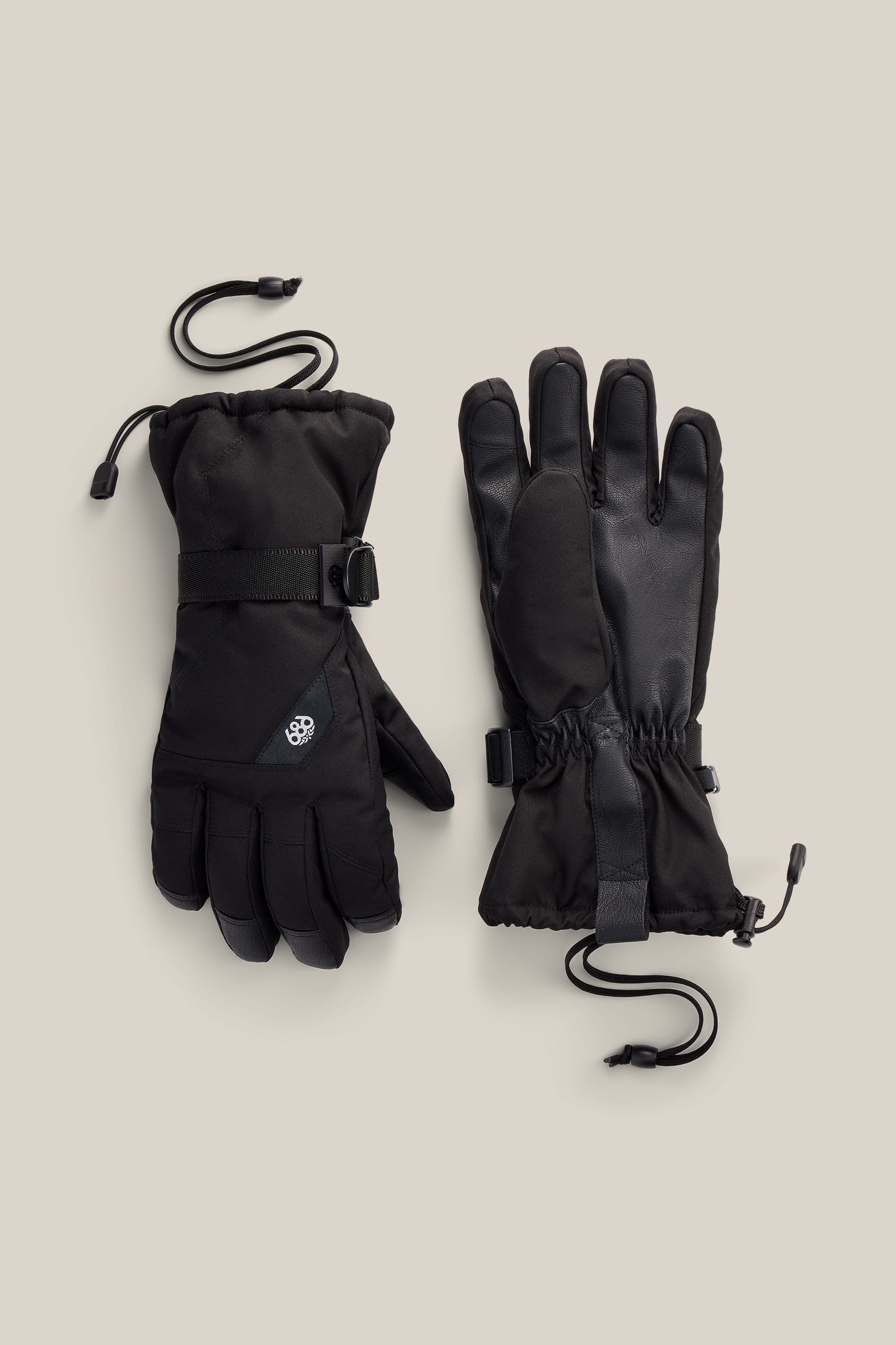 A pair of 686 Men’s Sightline™ Gloves in black, designed with adjustable wrist straps and attached drawstring cords, are shown against a plain light beige background. These insulated PU gloves by 686 offer both style and functionality to keep your hands warm all winter long.