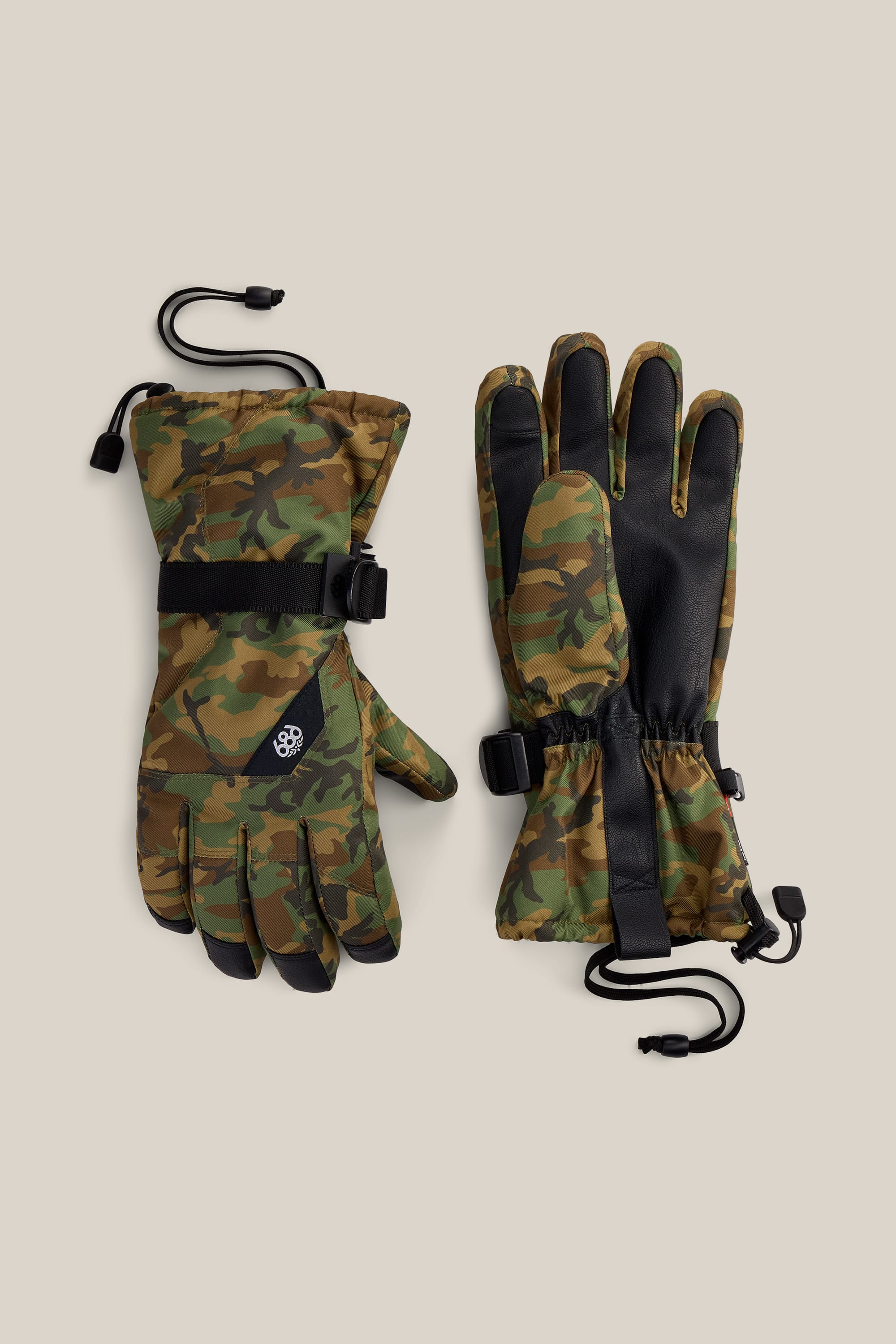 A pair of 686 Men’s Sightline™ Gloves in green camouflage feature black PU palms and adjustable straps. Designed for winter wear, these gloves include drawstrings at the wrists and display a small 686 logo on the back of one glove. The poly gloves are shown against a beige background.