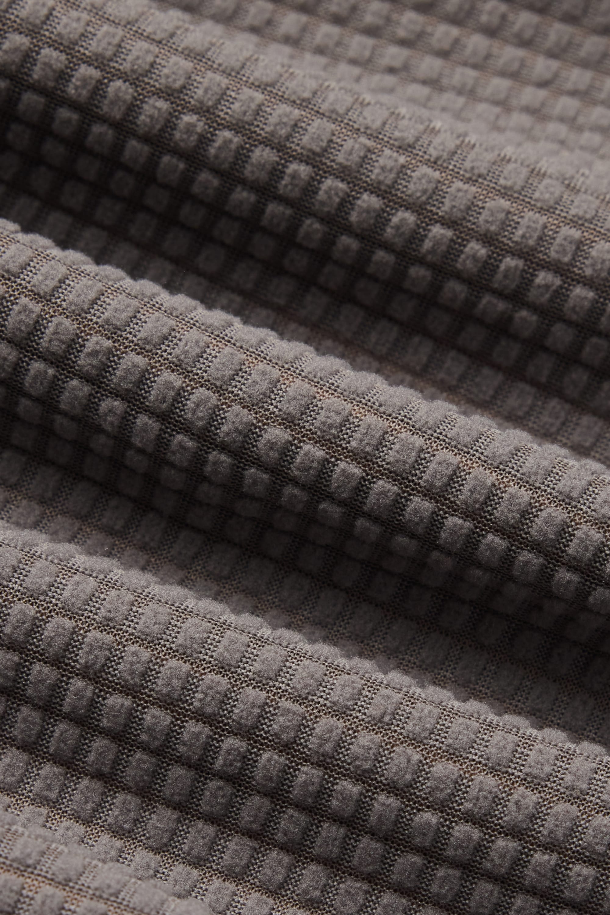 Close-up of gray fabric with a waffle texture, featuring a grid pattern and gentle diagonal folds—characteristic of the cozy 686 Men’s Mission Grid™ Raglan Hoody by 686.