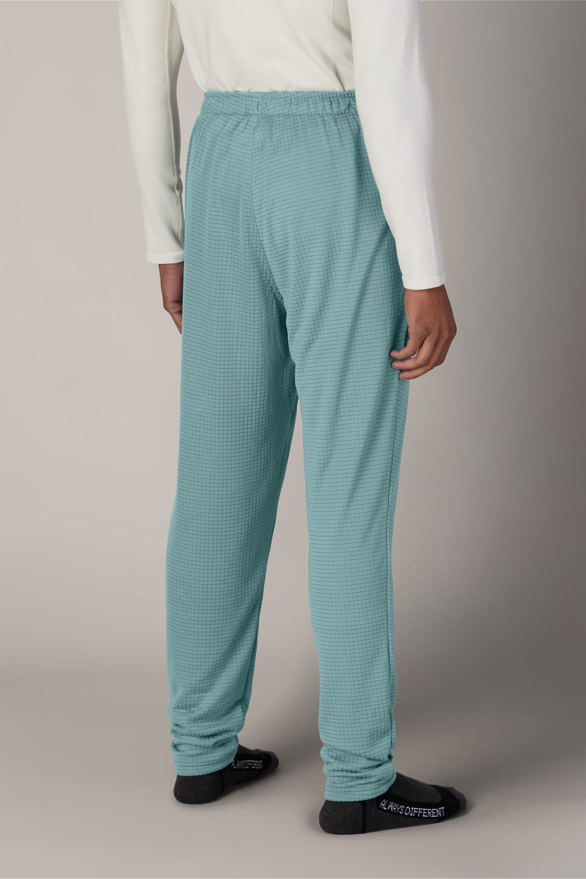 A person stands with their back to the camera, wearing 686 Men’s Mission Grid™ Pant in light blue, a white long-sleeve shirt, and black socks against a neutral background.