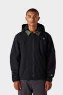 A person faces forward against a light grey background, wearing the 686 x Malbon Mens Caddie Performance Jacket by 686—a black hooded jacket with a front zipper and a small circular logo on the left chest.