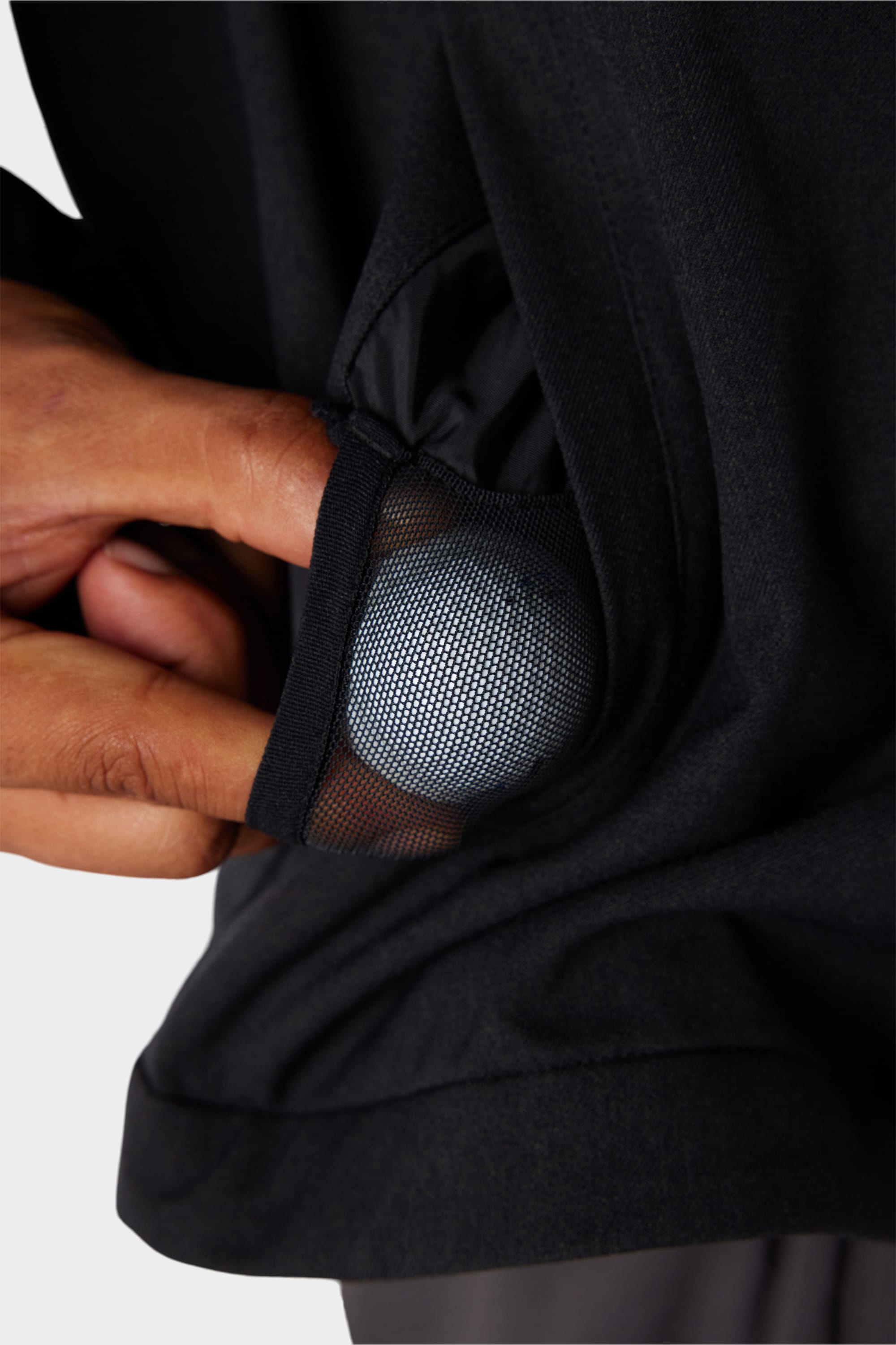 A hand reaches into the black mesh pocket of the 686 x Malbon Mens Caddie Performance Jacket, revealing a small, round device inside.