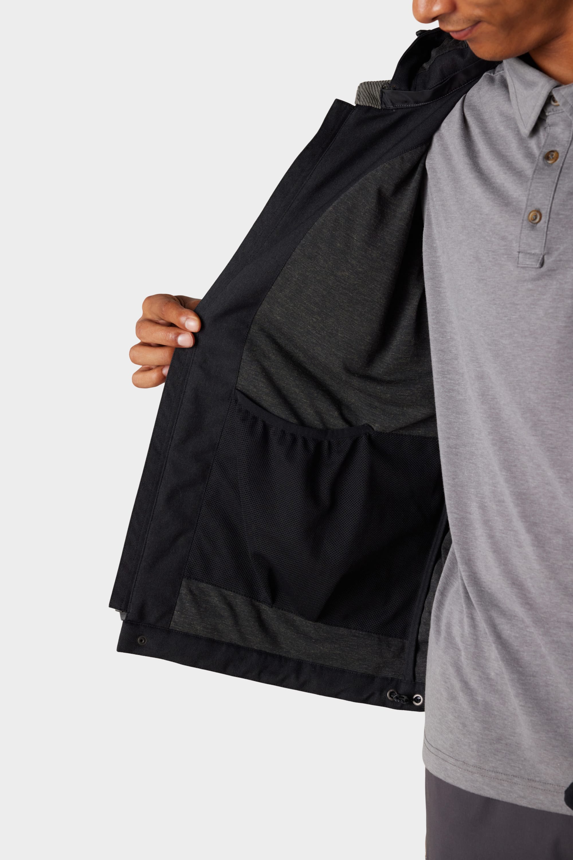 A person wearing a grey polo shirt holds open the 686 x Malbon Mens Caddie Performance Jacket by 686, displaying its interior pocket and lining, with only their lower face and upper body visible.