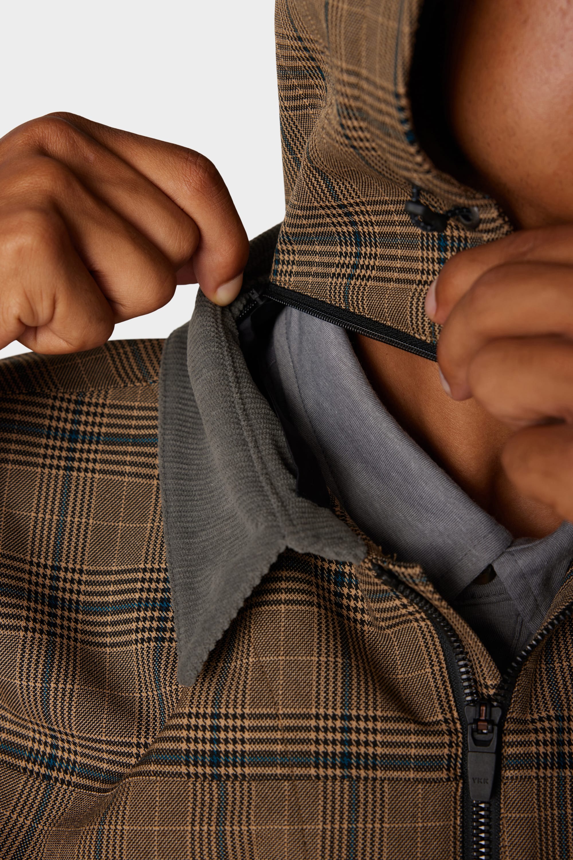 A person wearing the 686 x Malbon Mens Caddie Performance Jacket by 686 is unzipping it to reveal a grey collared shirt underneath. The photo focuses closely on the upper torso and hands.