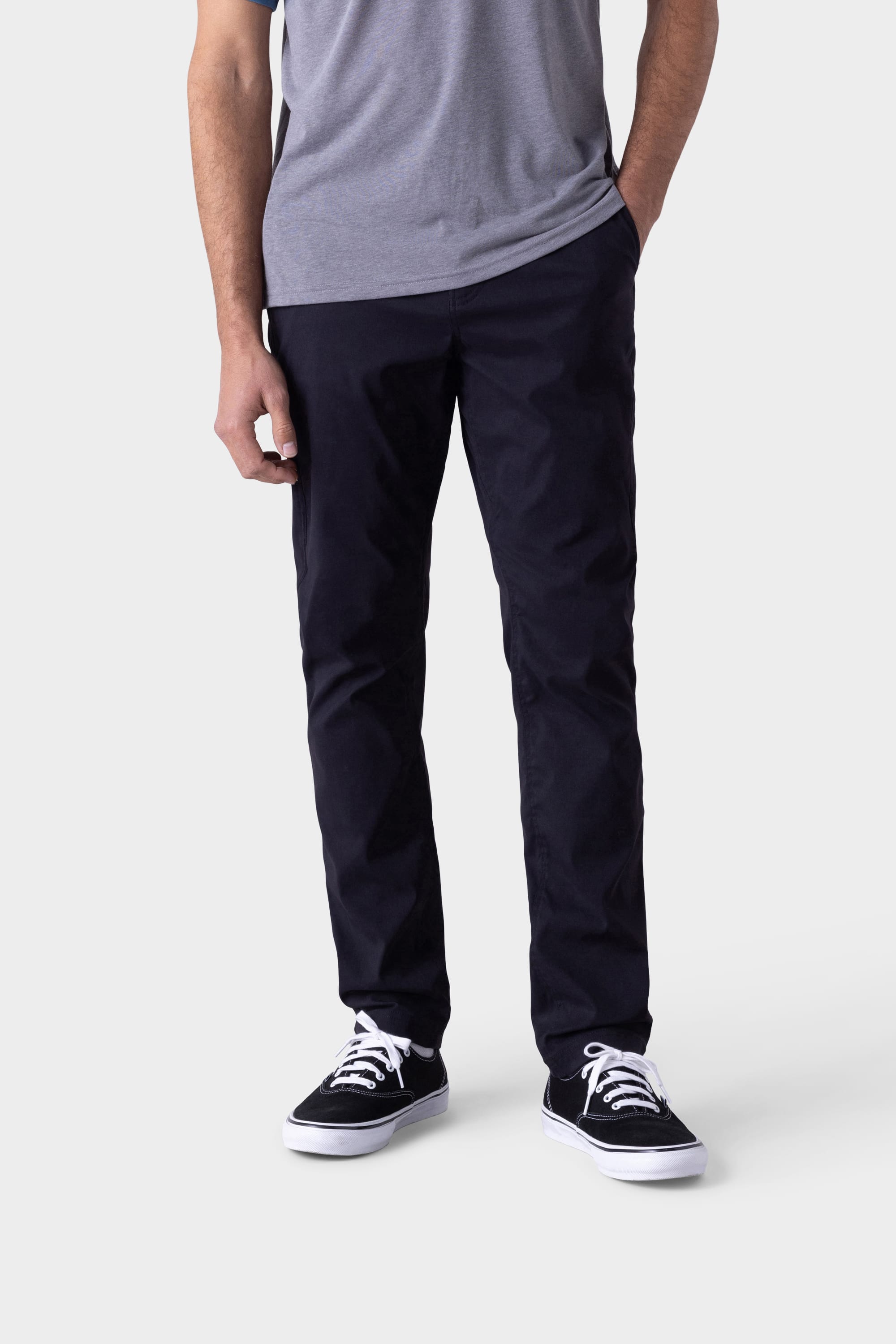 Against a plain light background, a person—face not visible—stands with one hand in their pocket wearing the 686 Mens Platform Bike Pant - Slim Fit in dark navy, a grey t-shirt, and black-and-white sneakers.