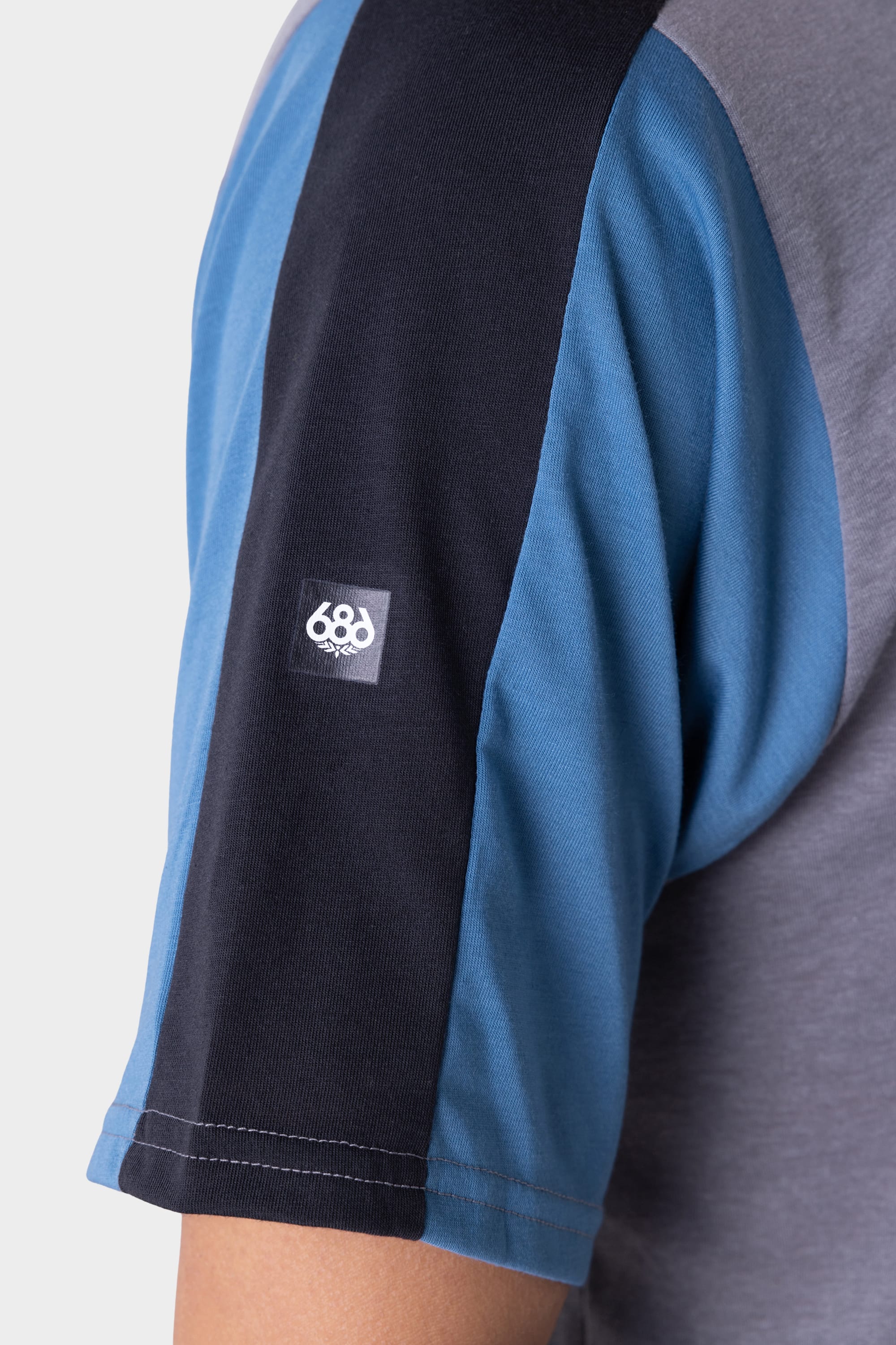 Close-up of a persons upper arm in the 686 Mens Rival Short Sleeve Bike Jersey, featuring blue, black, and grey color blocks and a small white 686 logo patch on the sleeve.