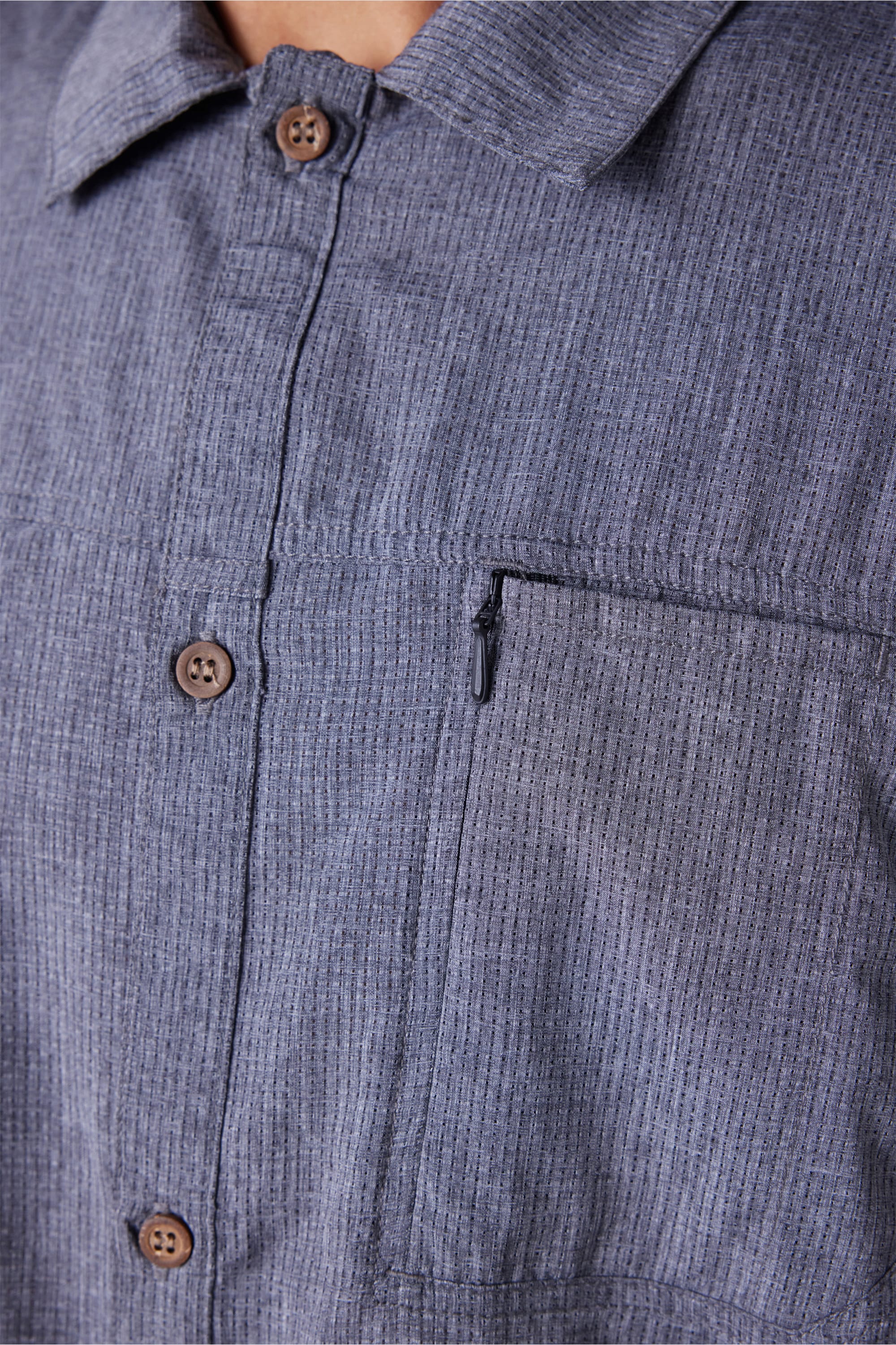 Close-up of the 686 Mens Seeker Perforated Button Up shirt in blue-grey with vertical stripes, brown buttons, and a zippered left chest pocket. Only the upper torso is shown.