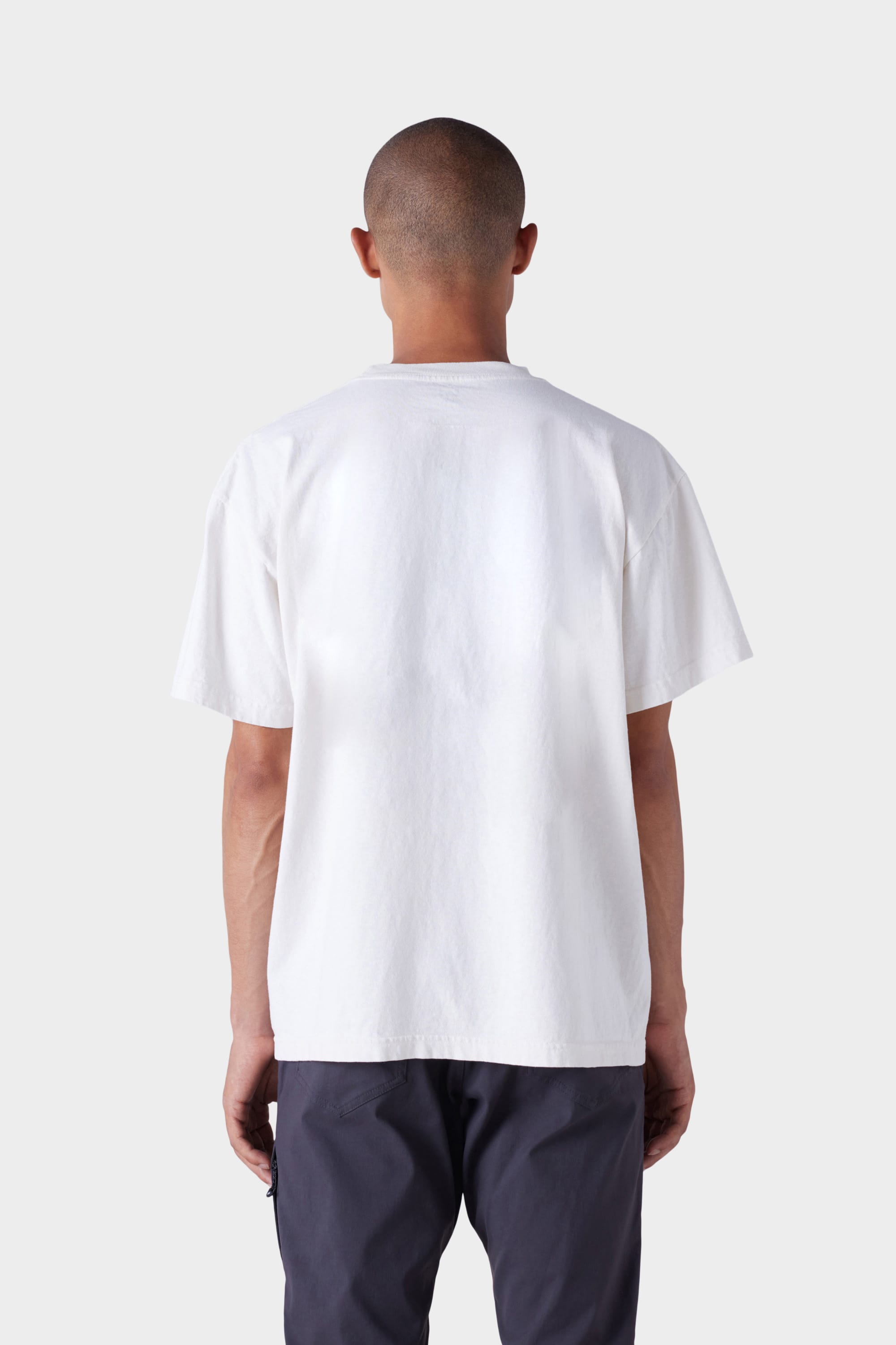 A person with short hair is facing away, wearing the 686 Mens Under the Summer Sun Short Sleeve Tee by 686 and dark pants, against a light grey background.