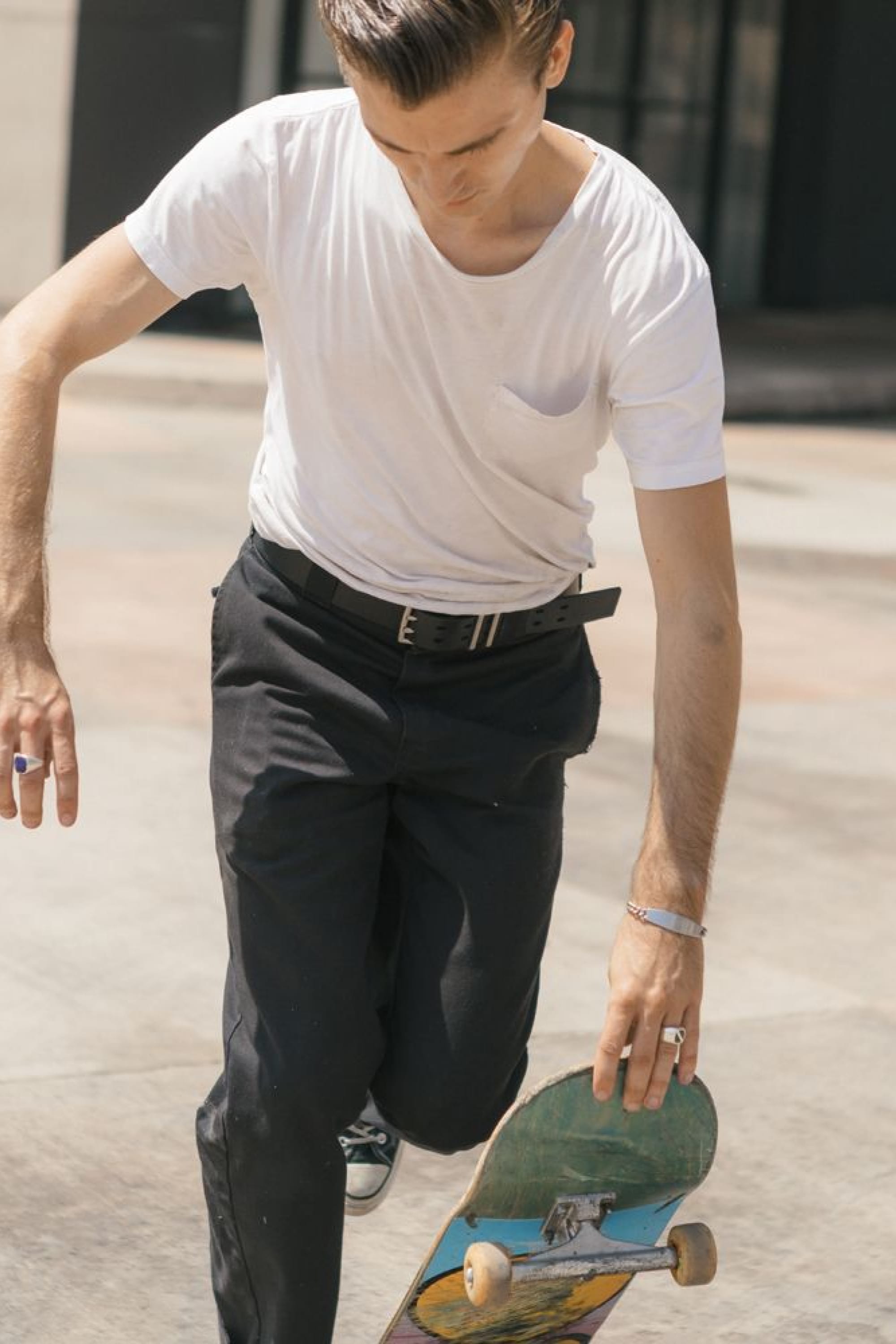 Wearing a white t-shirt and black pants, someone readies for a skateboard trick while sporting the Westwell 686 Westwell Voyager Belt on a sunny day.