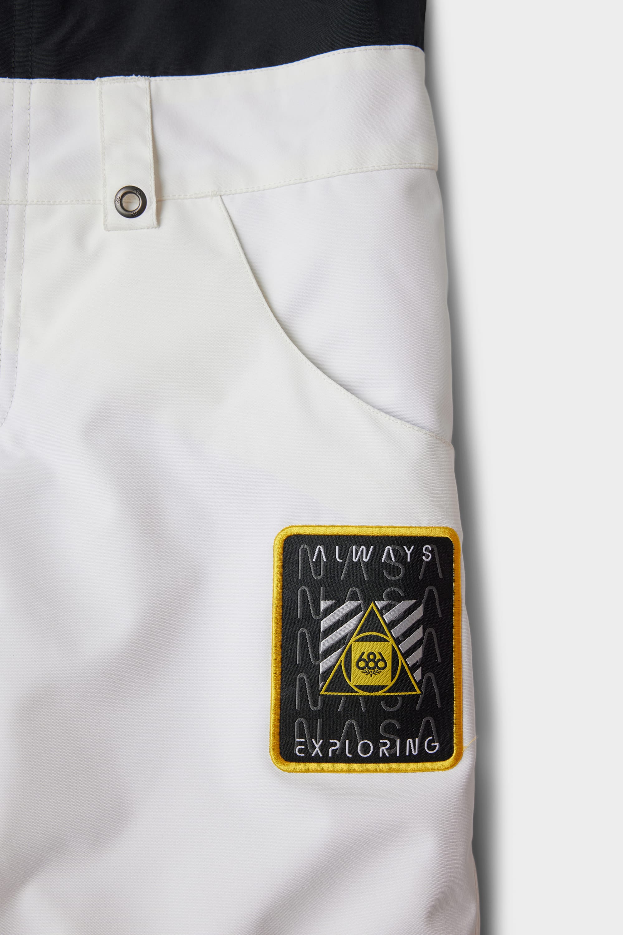 Close-up of the 686 Youth Exploration Insulated Bib by 686, featuring a front pocket, silver button, and a rectangular patch with a yellow triangle, mountain design, and ALWAYS EXPLORING in black and yellow.