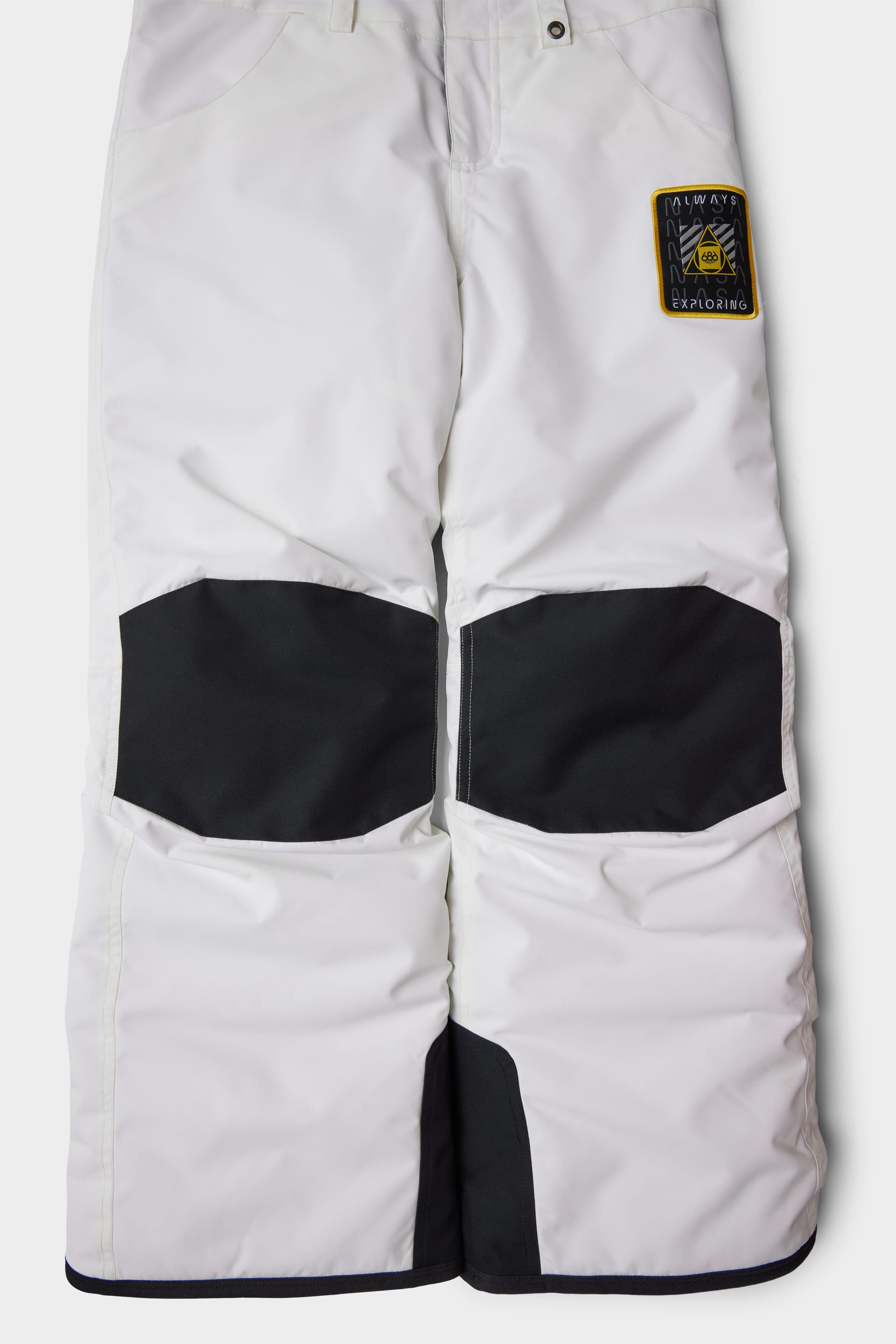 The 686 Youth Exploration Insulated Bib by 686 features white fabric, black reinforced knee patches, a black and yellow patch on the right thigh, pockets, and visible stitching details.