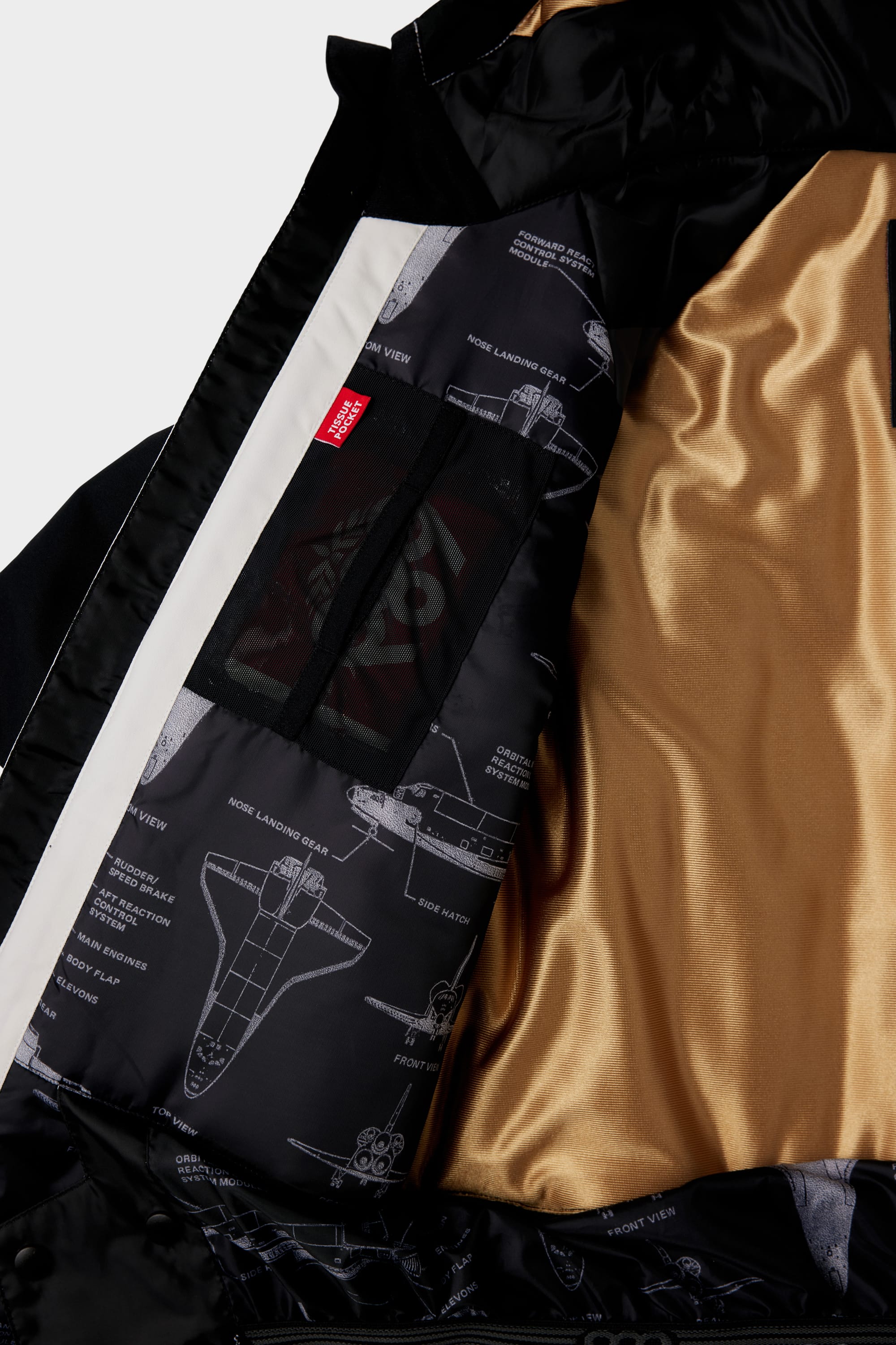 Close-up of the 686 Youth Exploration Insulated Jacket’s interior: gold satin lining, black section with white spacecraft technical drawings and labeled diagrams, plus a visible red tag.
