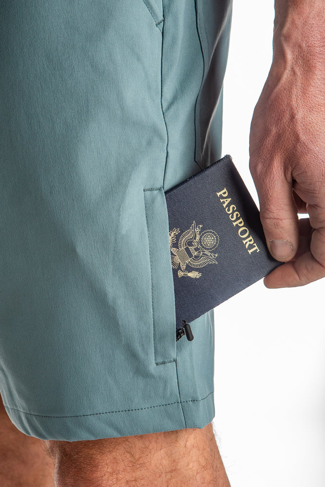 A close-up of a hand placing a dark blue U.S. passport into the zippered pocket of breathable, light blue-green 686 Mens Everywhere Hybrid Short by 686.