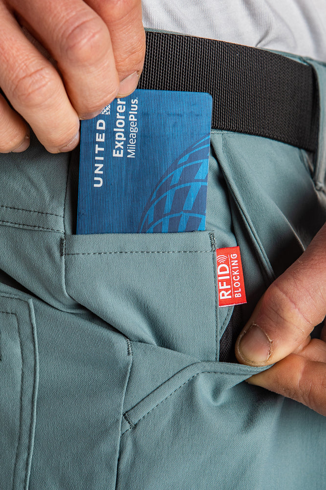 A person slips a blue United Explorer credit card into the front pocket of teal 686 Mens Everywhere Hybrid Shorts by 686, which are breathable, stain-resistant, and feature a red RFID blocking tag.