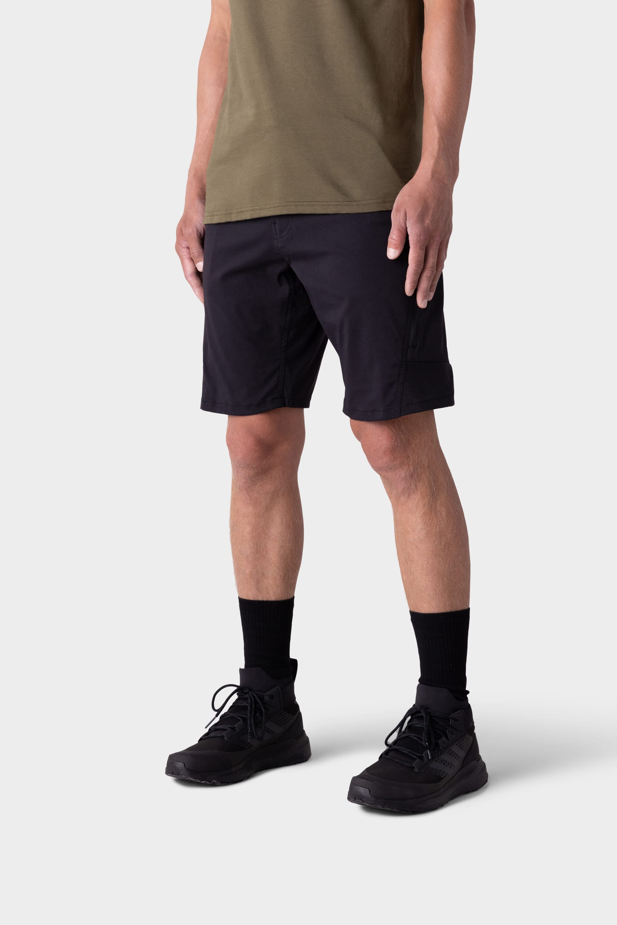 A person stands against a plain background, wearing a khaki green T-shirt, black socks, black athletic shoes, and 686 Mens Anything Hybrid Cargo Short by 686. The image is cropped from shoulders to feet.