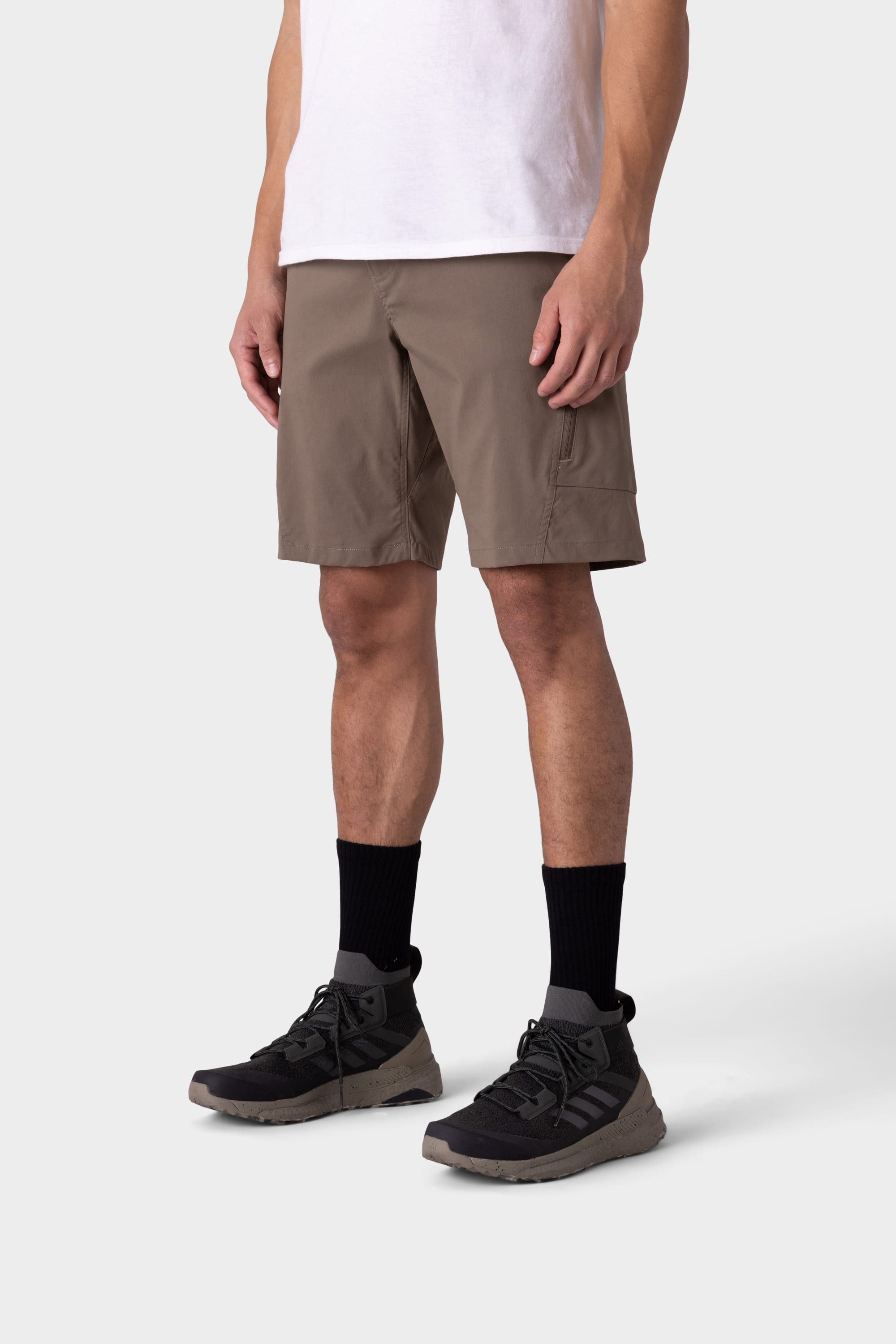 A person wearing a white T-shirt, 686 Mens Anything Hybrid Cargo Short in taupe, black crew socks, and black athletic shoes stands against a plain light background. The image, cropped at the shoulders, highlights minimalist style.