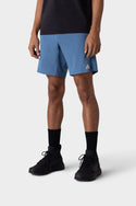 A person is shown from the neck down, standing against a plain light background, wearing a black T-shirt, 686 Mens ATP Stretch Performance Shorts in blue, black crew socks, and black sneakers.