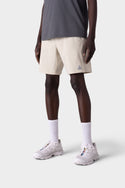 A person wearing a dark gray t-shirt, 686 Mens ATP Stretch Performance Shorts in light beige, white crew socks, and white running shoes stands against a plain white background. The image is shown from the shoulders down.