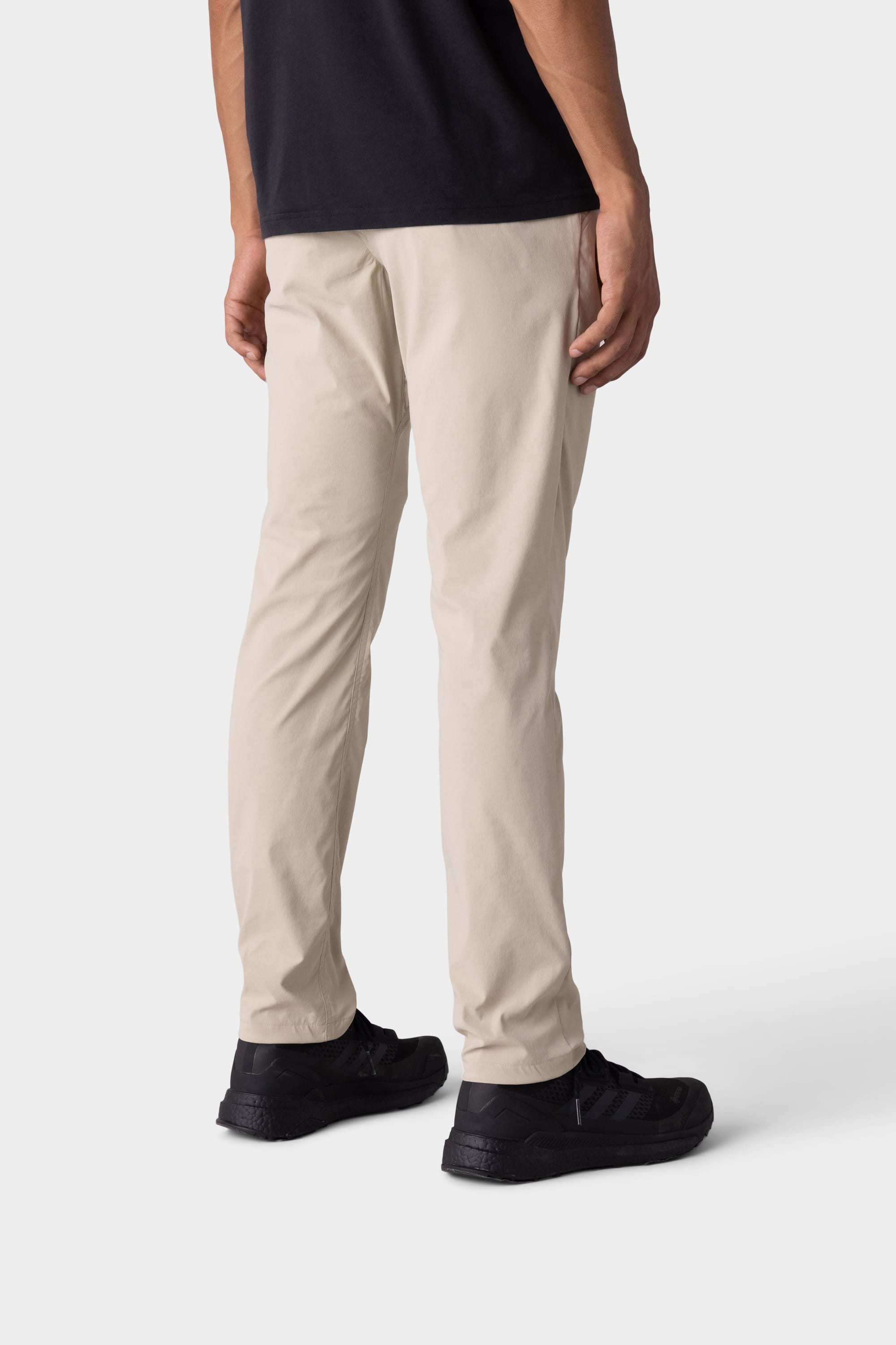 A person models the 686 Mens Everywhere Featherlight Chino Pant - Slim Fit in beige, paired with a black shirt and sneakers on a white background—ideal for summer wardrobes or warm weather outings.