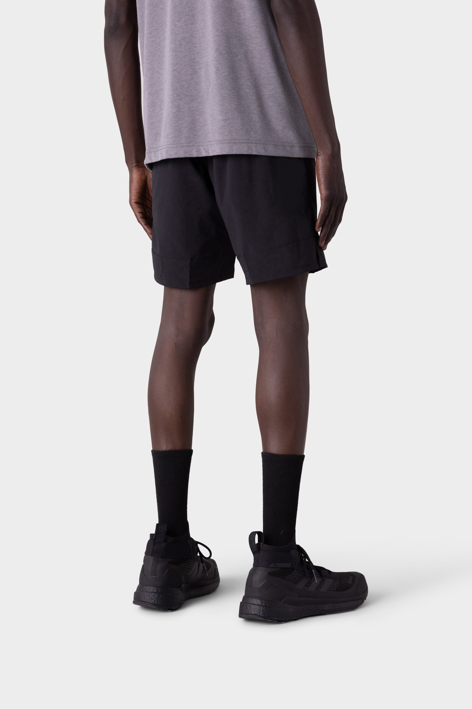 A person stands with their back to the camera, wearing a gray t-shirt, black crew socks, black sneakers, and 686 Mens ATP Stretch Performance Short by 686 against a plain light background.