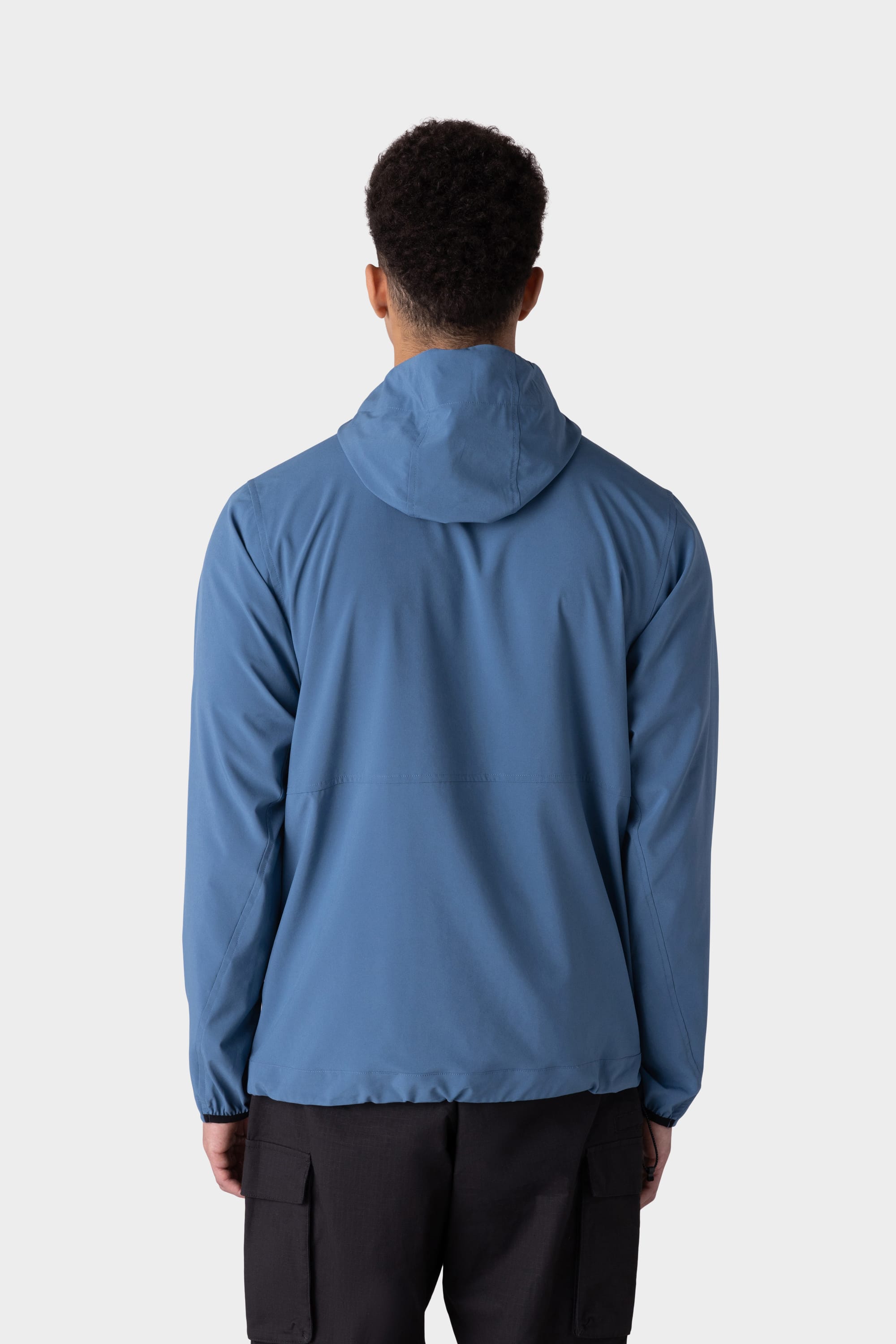 A person with short curly hair is shown from behind, wearing the 686 Mens ATP Stretch Wind Jacket in blue and black cargo pants against a plain light gray background.