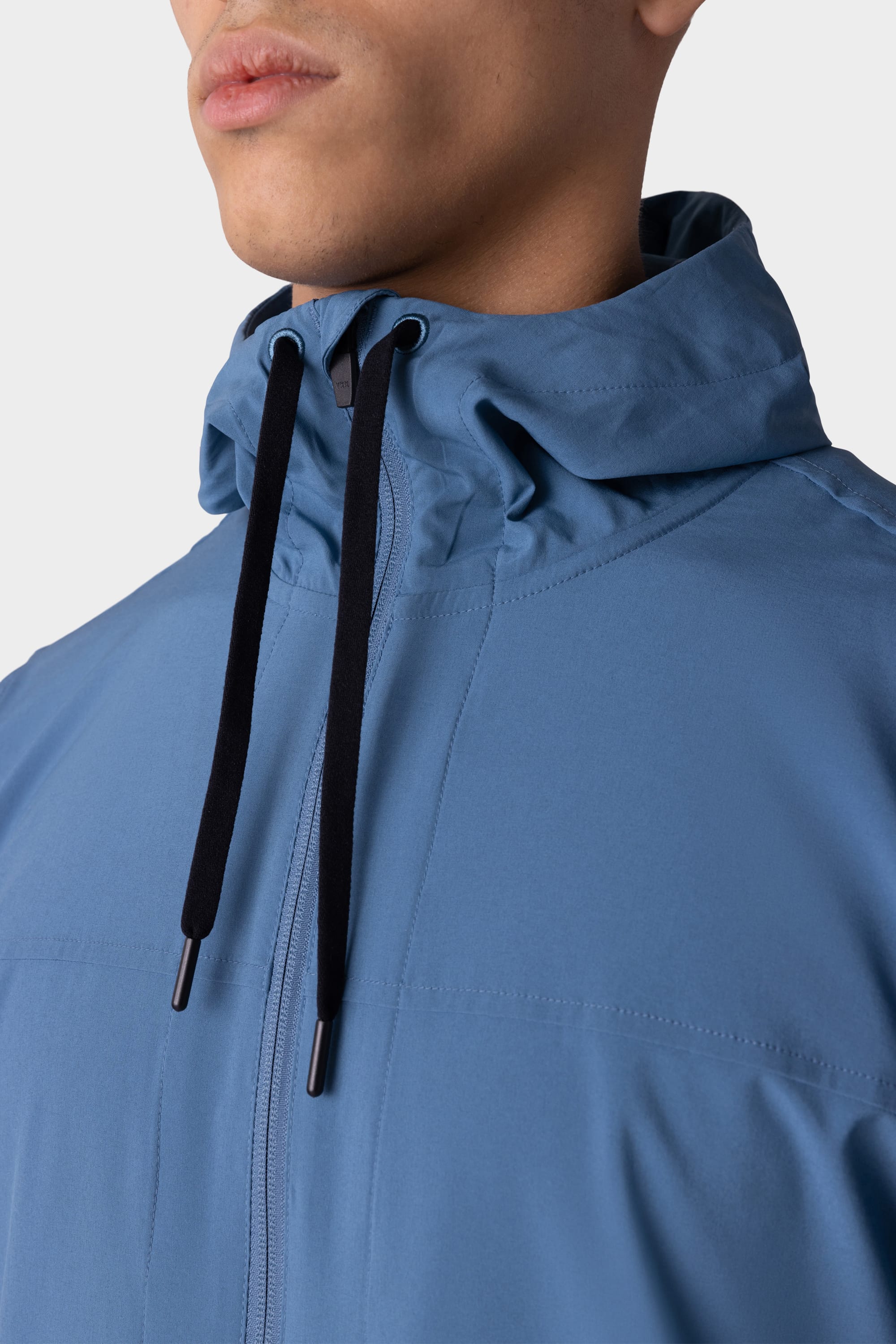 A close-up of a person wearing the 686 Mens ATP Stretch Wind Jacket, featuring black drawstrings and highlighting the jacket’s upper chest, shoulders, and part of the face against a plain background.