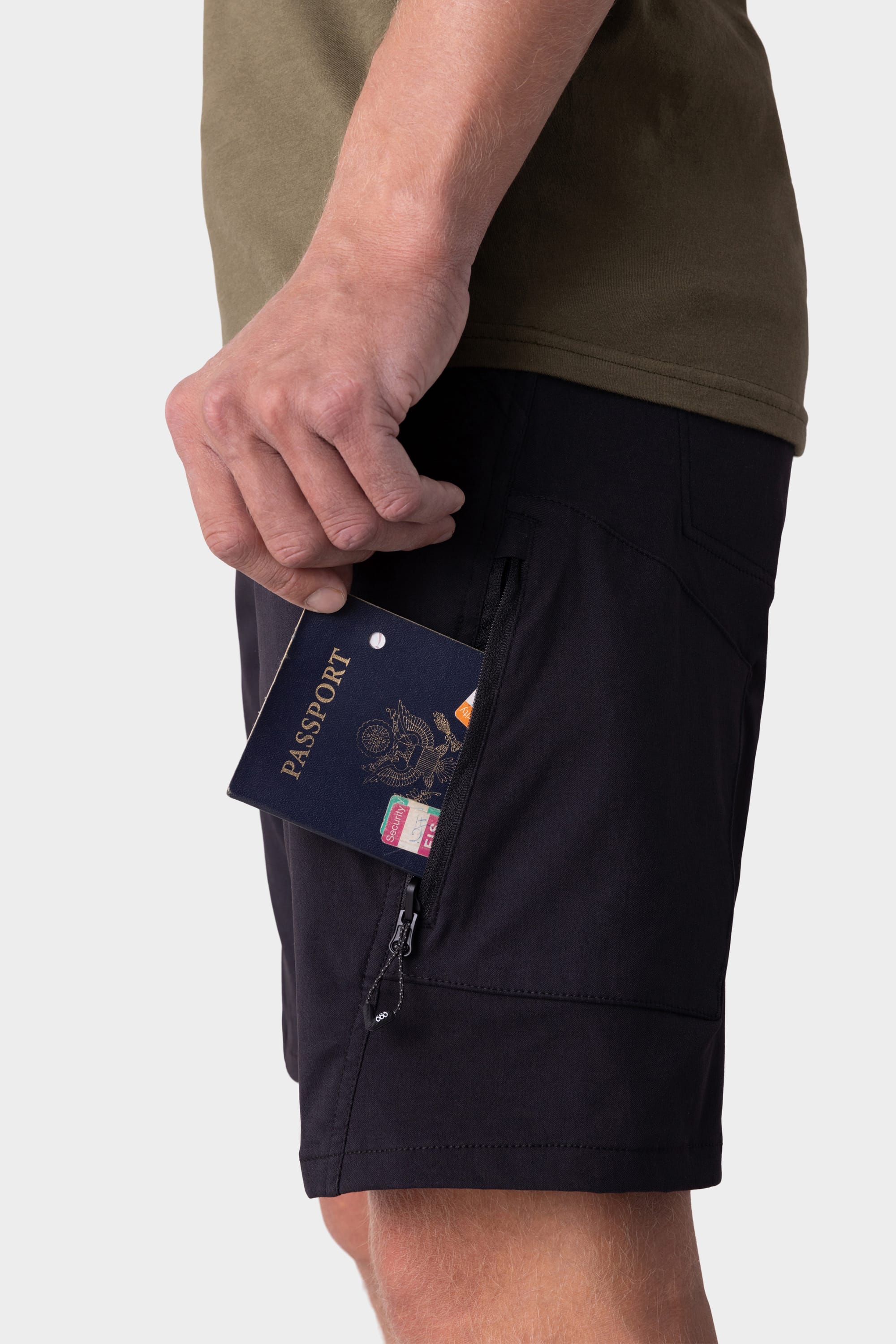 A person in 686 Mens Anything Hybrid Cargo Short places a passport and cards into the zippered side pocket, while their olive green shirt is partially visible.