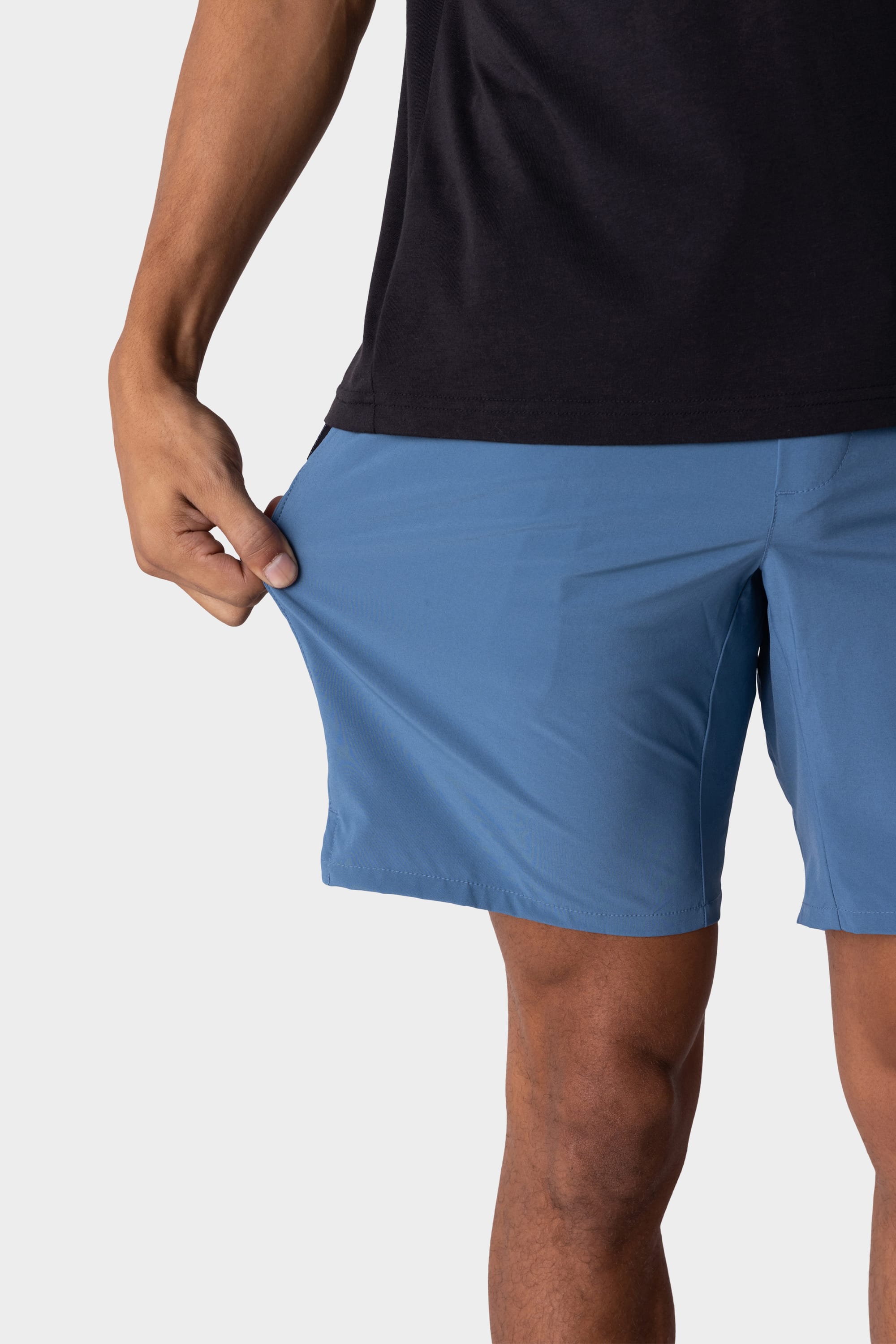 A person wearing a black shirt and blue 686 Mens ATP Stretch Performance Short stretches the shorts’ fabric outward with their left hand to demonstrate its flexibility.
