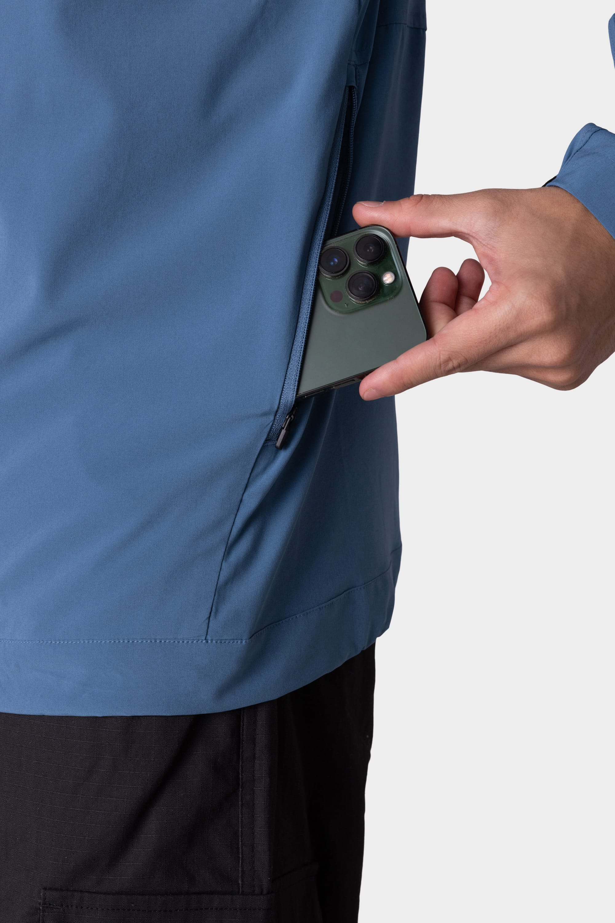 A man wearing the 686 Mens ATP Stretch Wind Jacket is placing a green smartphone with three camera lenses into the jacket’s zippered pocket.