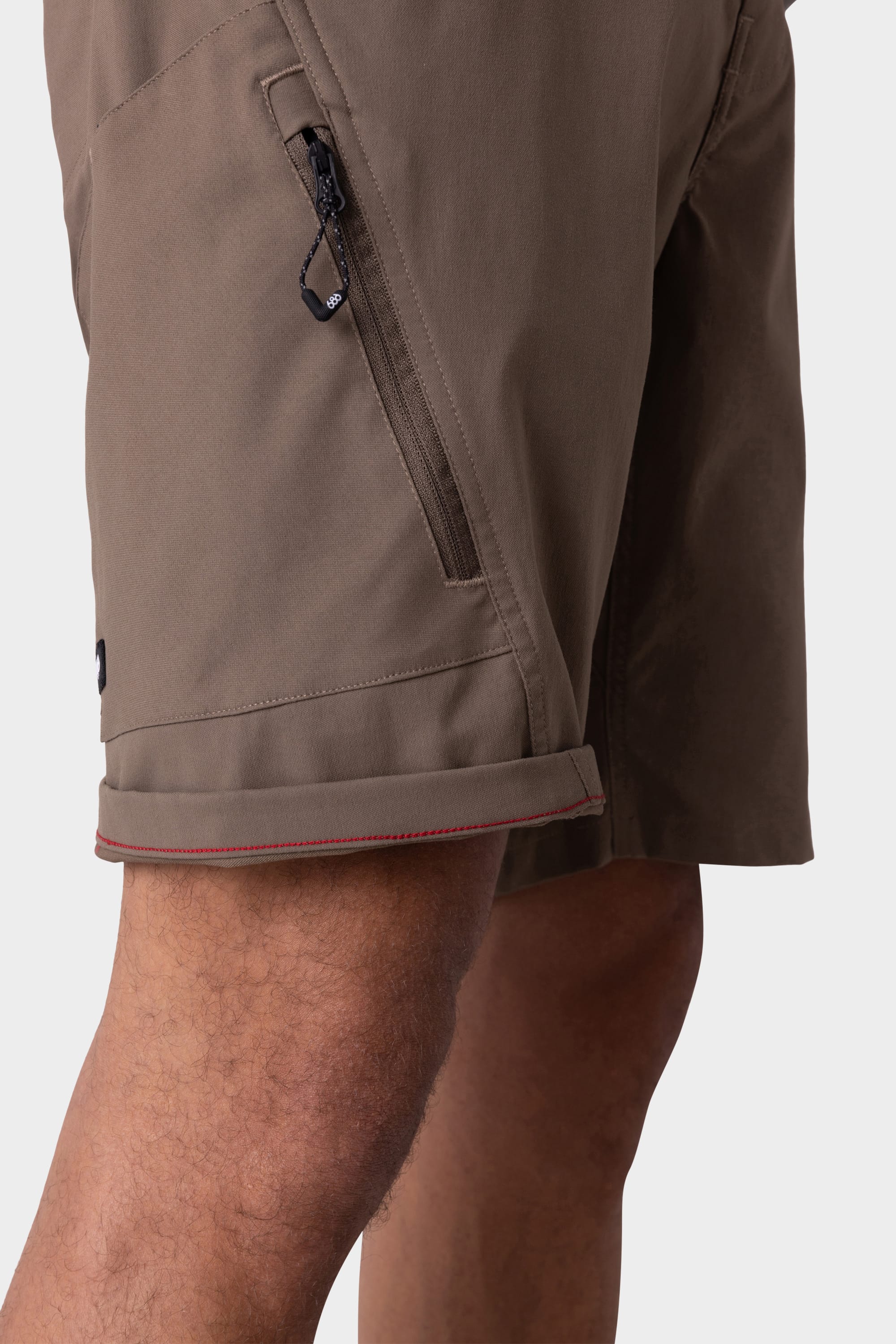 A close-up of a person wearing the 686 Mens Anything Hybrid Cargo Short, featuring a minimalist design, zippered side pocket, rolled hem, and visible stitching details. Brand: 686. Part of their upper leg and knee is also shown.