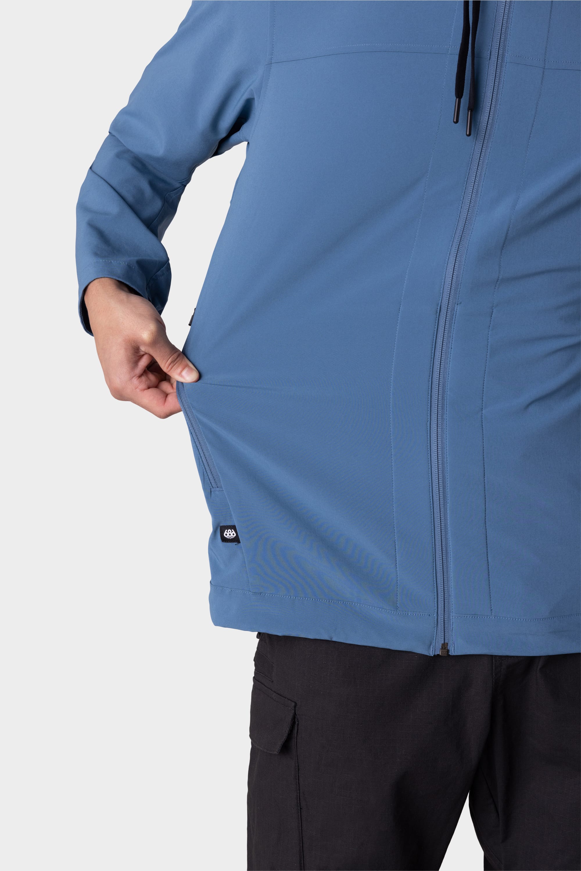 A person wearing the 686 Mens ATP Stretch Wind Jacket in blue stretches the side, demonstrating the flexibility of this 686 jacket.