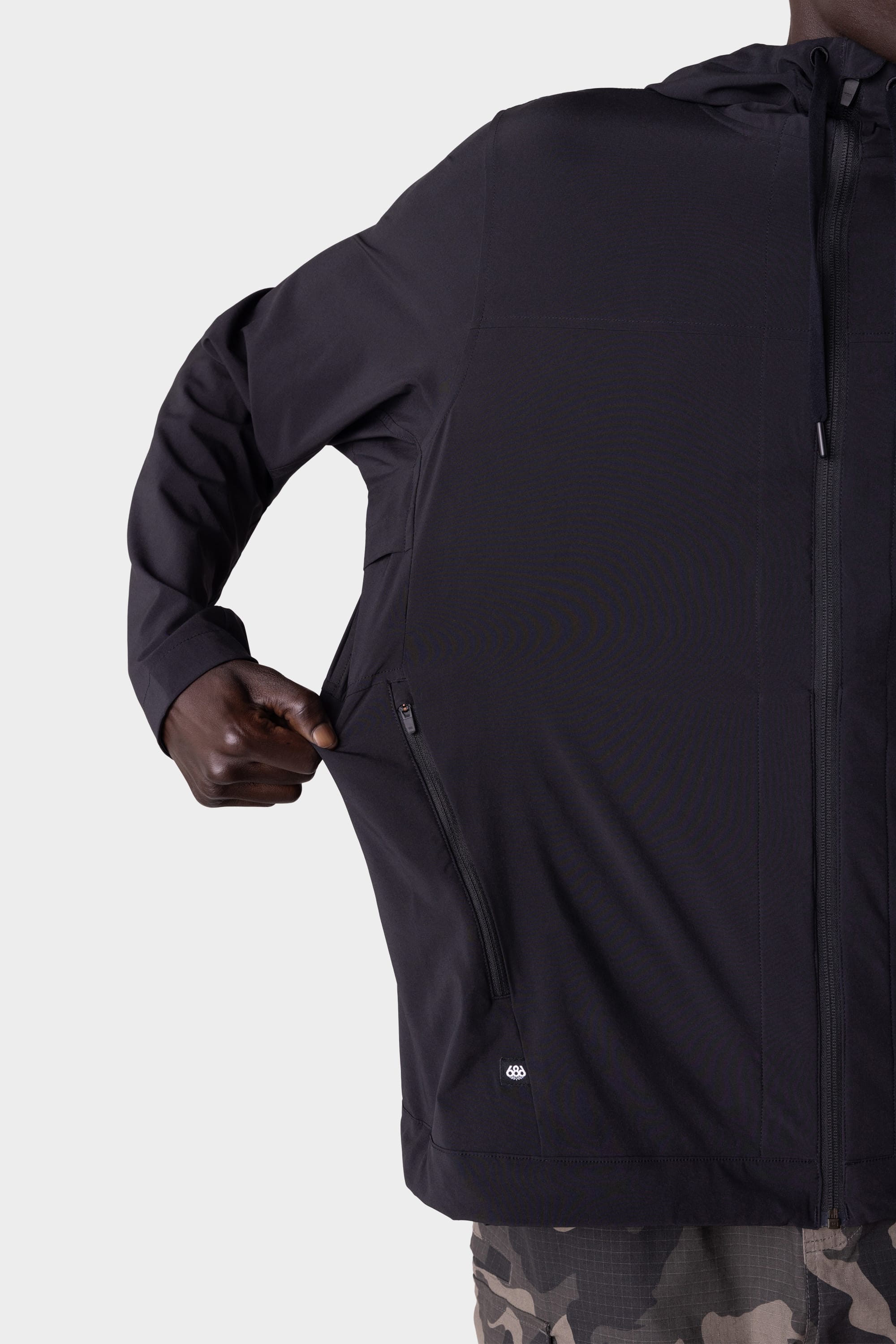 A person wearing the 686 Mens ATP Stretch Wind Jacket in black unzips a side pocket; only the right half of their upper body is visible against a plain background.