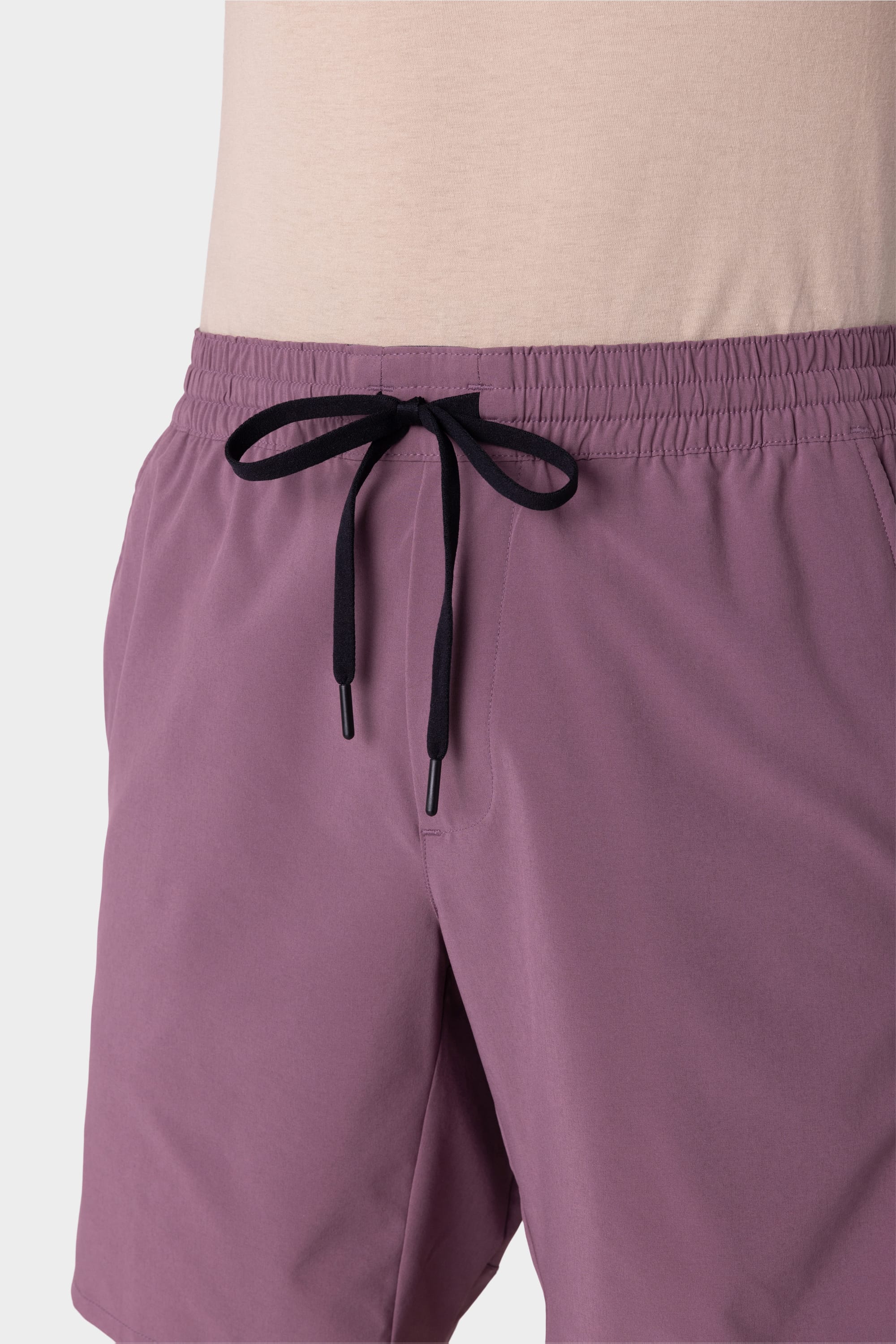A person is wearing 686 Mens ATP Stretch Performance Short by 686 in light purple, featuring an elastic waistband and black drawstring, paired with a light beige top. The photo shows from midsection to just above the knees.