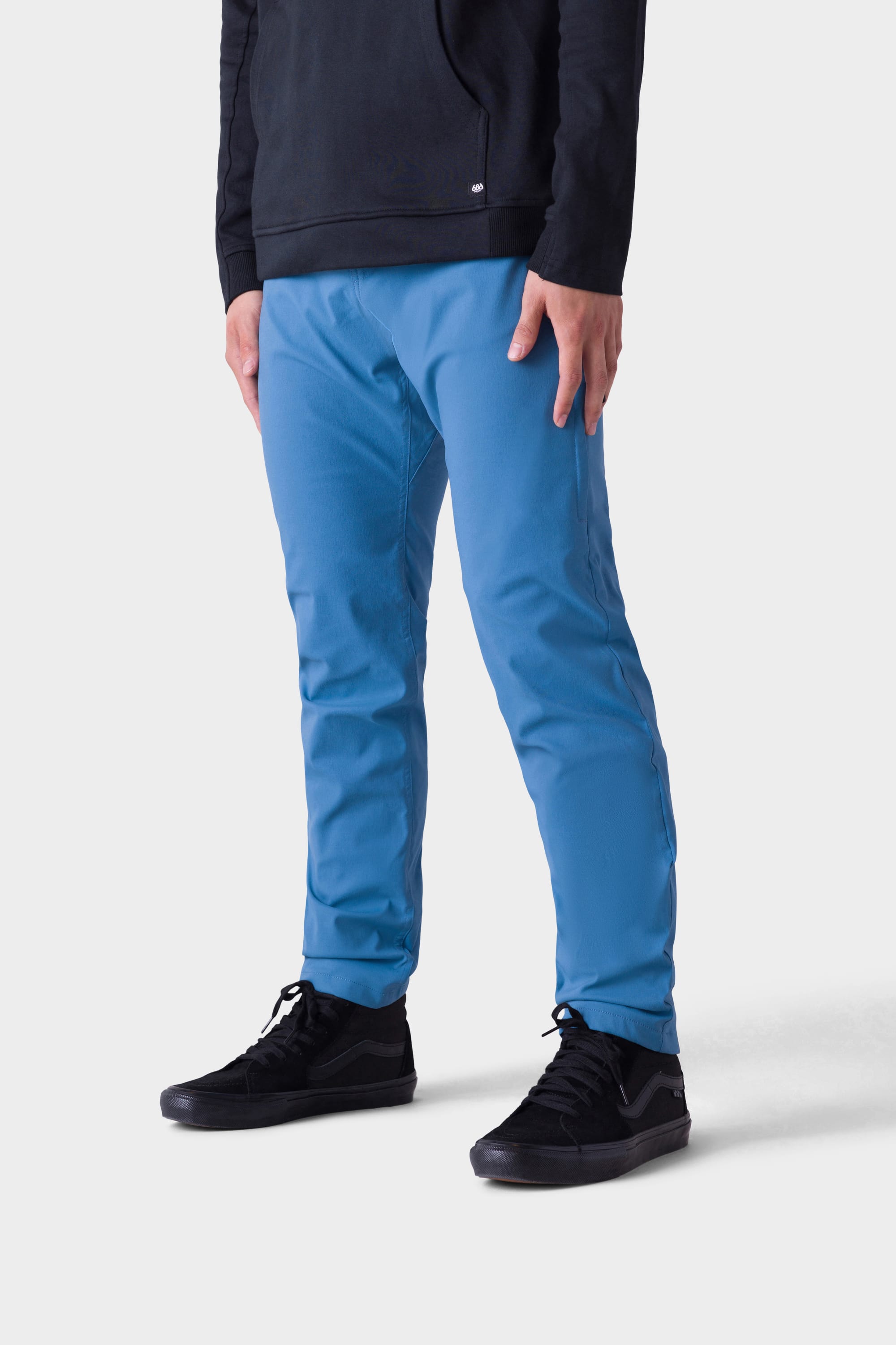 A person, shown from the shoulders down against a light background, wears the 686 Mens Everywhere Merino-Lined Pant - Slim Fit in bright blue, pairing it with a black long-sleeve top and black sneakers for warmth in colder weather.