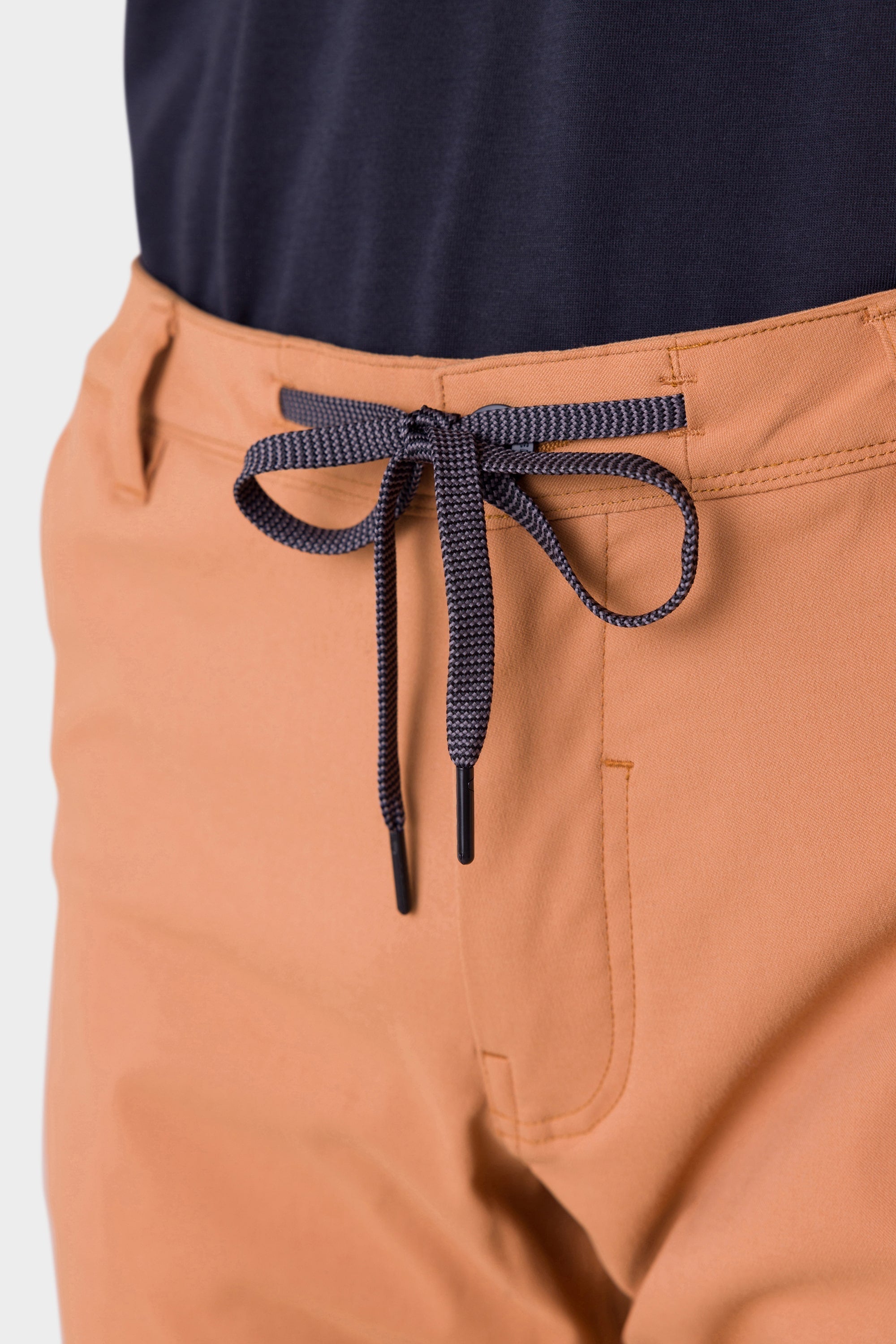Close-up of a person wearing 686 Mens Everywhere Merino-Lined Pant - Slim Fit in light orange with a dark blue drawstring, paired with a dark navy shirt—perfect for staying warm and comfortable in colder conditions.