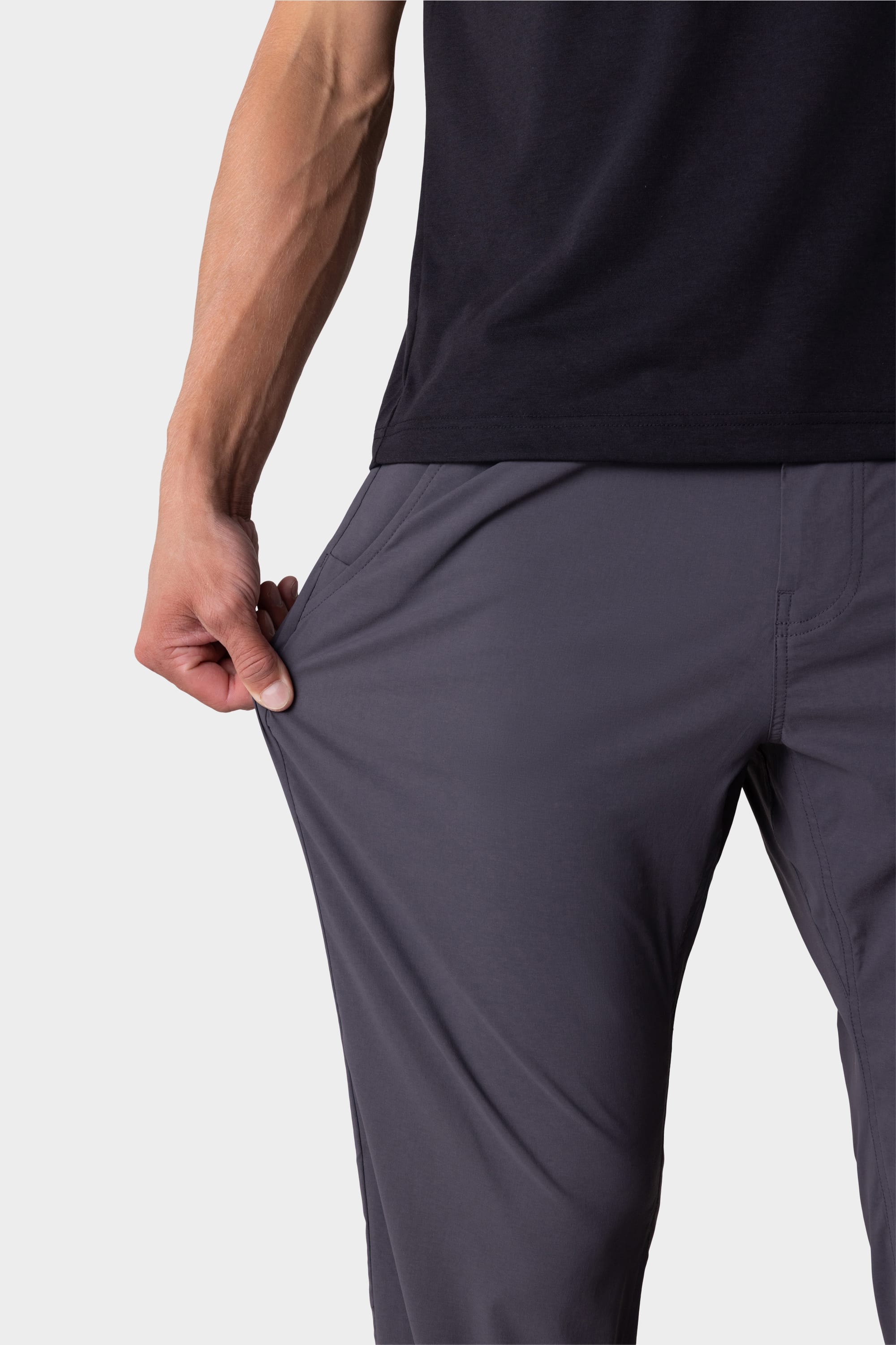 A person wearing a black shirt and 686 Mens Everywhere Featherlight Chino Pant - Relaxed Fit in gray stretches the fabric with one hand, demonstrating the flexibility of these 686 chinos.