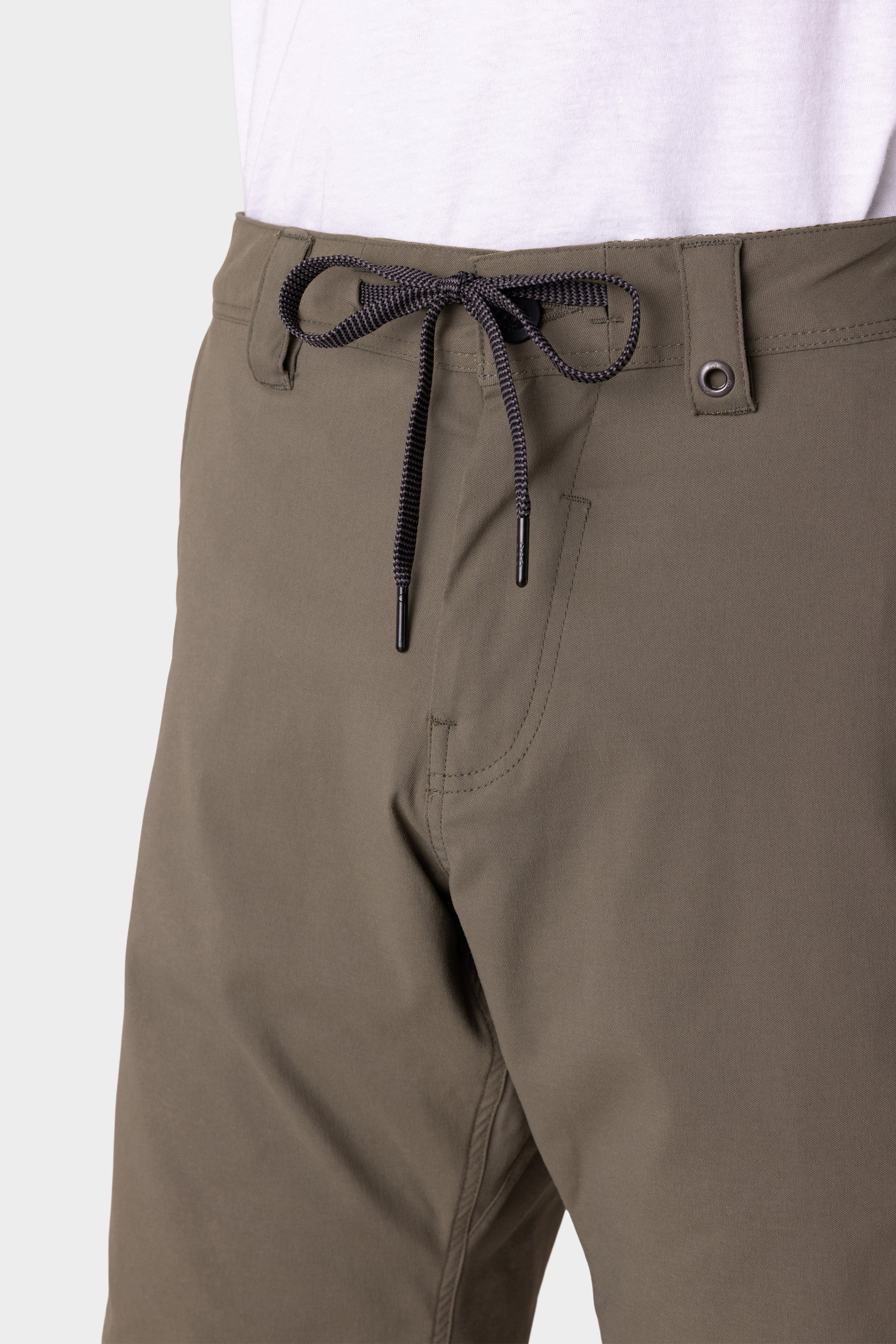 A close-up of a person wearing the 686 Mens Anything Hybrid Cargo Short in olive-green with a black and white drawstring, visible stitching, metal waistband button, and minimalist design, paired with a white shirt. Brand: 686.