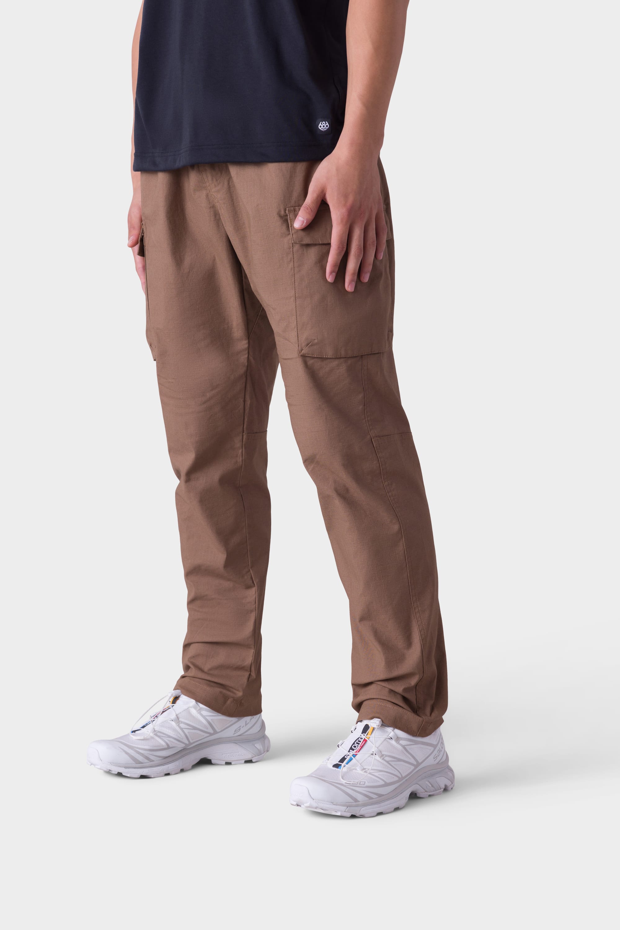 A person wearing 686 Mens All Time Cargo Pant - Wide Tapered Fit stands against a plain white background, with only the lower half of the body visible.