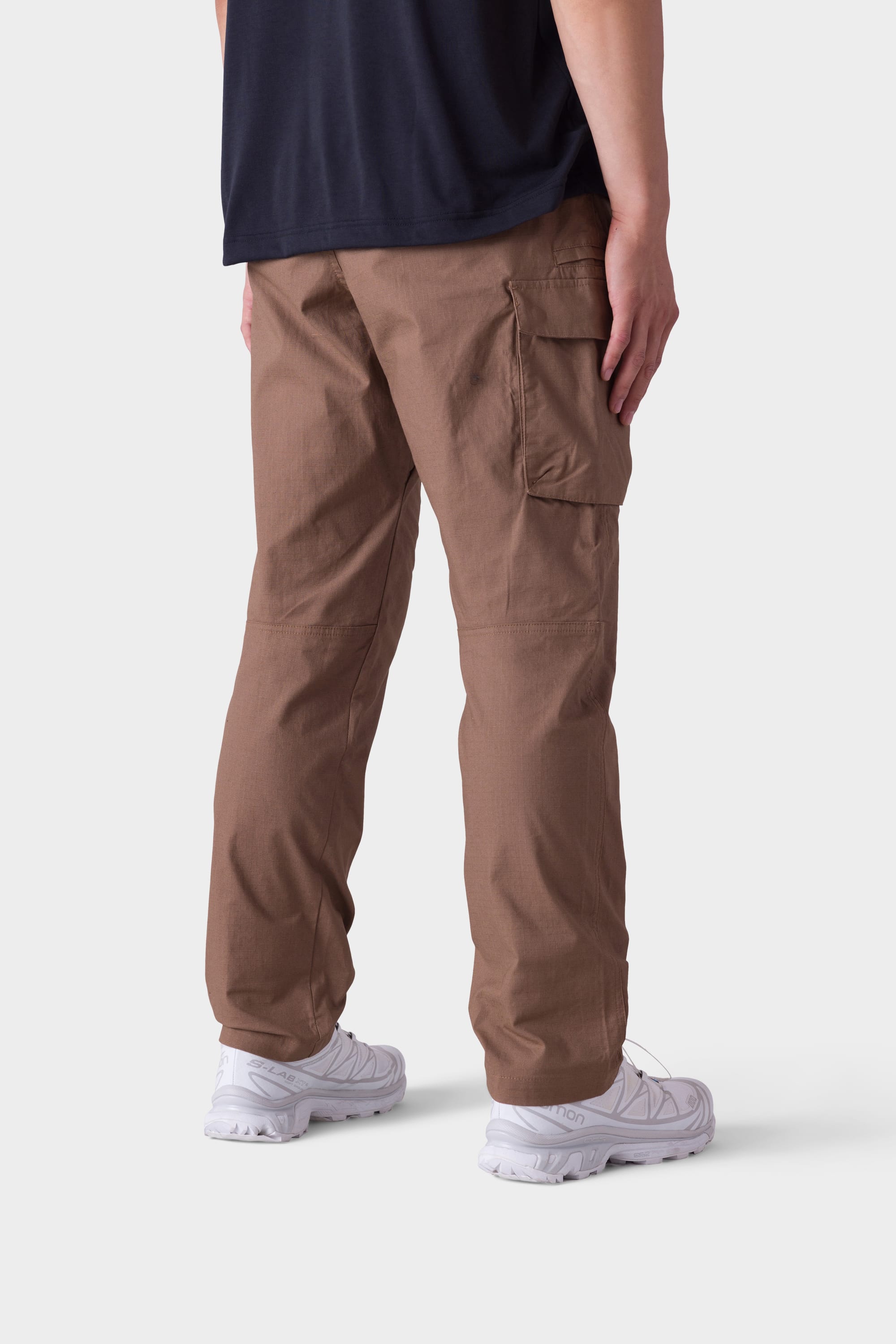 A person is seen from the back and side wearing the 686 Mens All Time Cargo Pant - Wide Tapered Fit by 686, paired with a black shirt and white sneakers, standing against a plain light background.