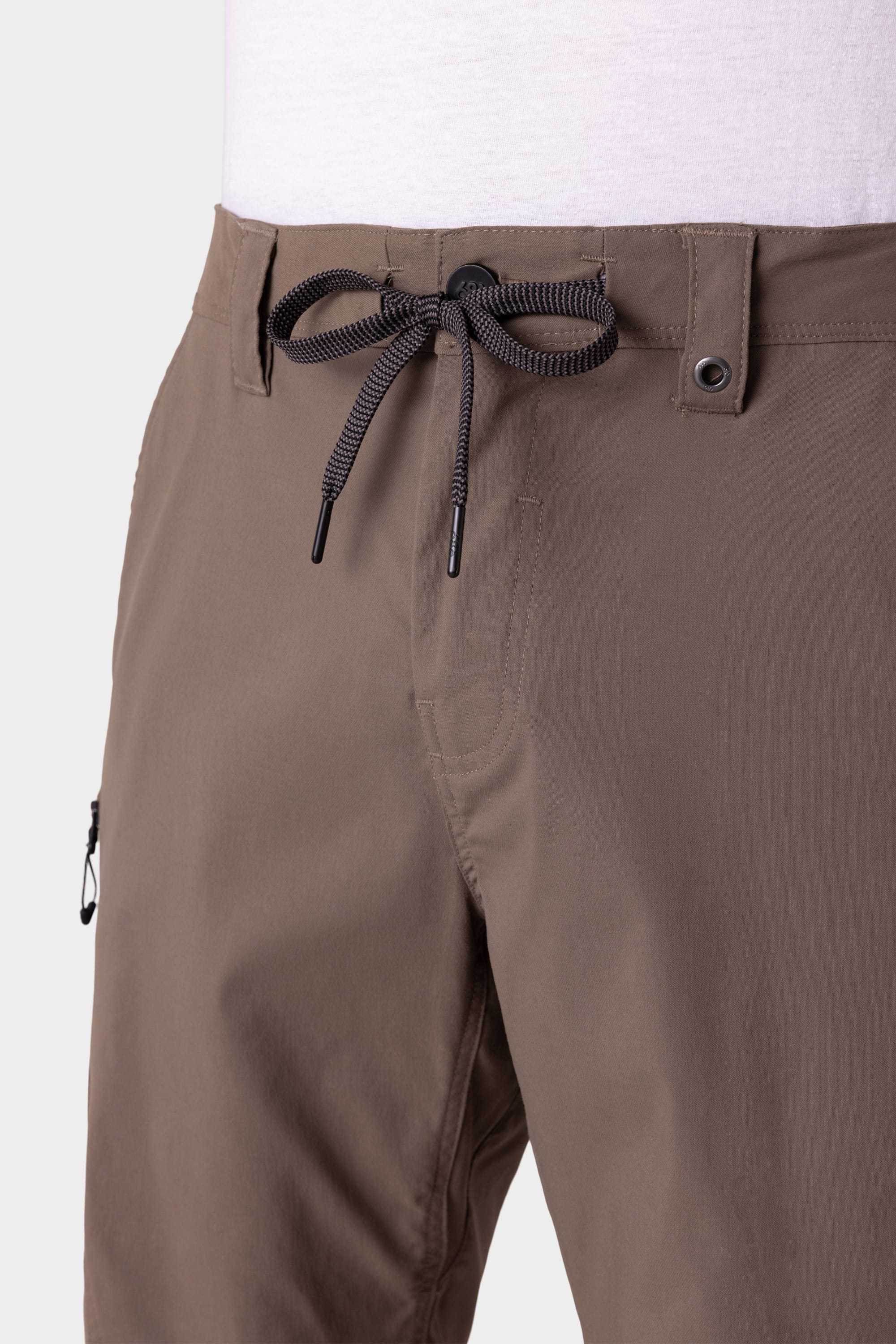 Close-up of a person wearing the 686 Mens Anything Hybrid Cargo Short in light brown, featuring a black and white drawstring waist, belt loops, button closure, and minimalist design by 686, paired with a white shirt for a clean, modern look.
