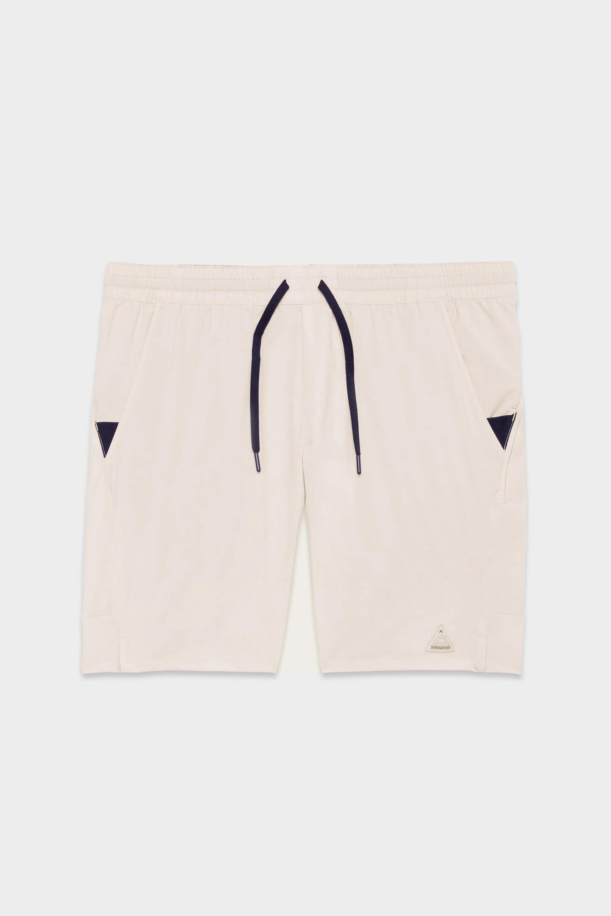 The 686 Mens ATP Stretch Performance Short by 686 features an off-white color, elastic waistband with dark drawstring, two side pockets with small dark triangular accents, and a subtle logo near the left hem.
