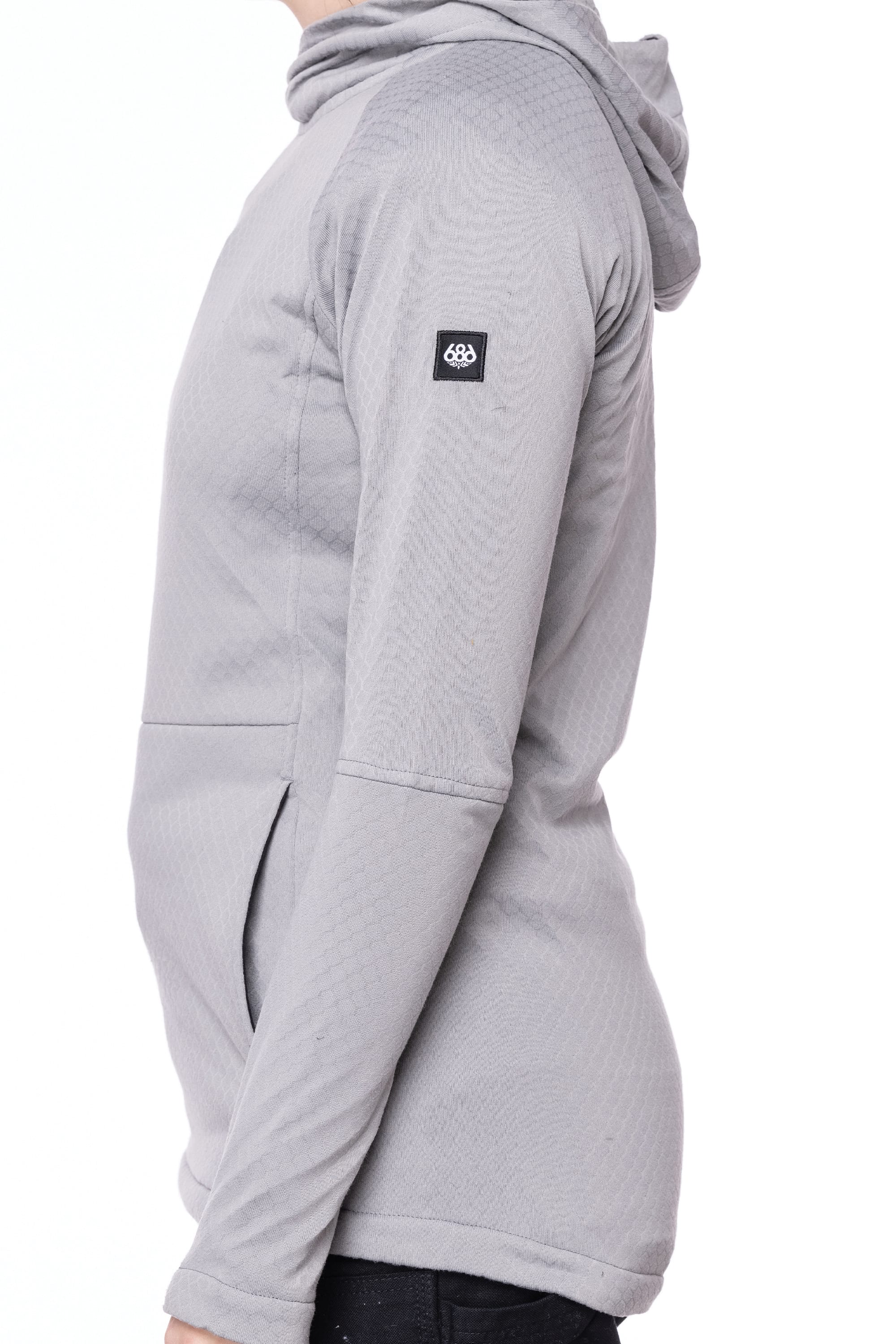 A person wearing the 686 Womens Mission Grid Fleece Hoody in light grey, featuring a black logo patch on the upper sleeve, is shown from the side against a white background.