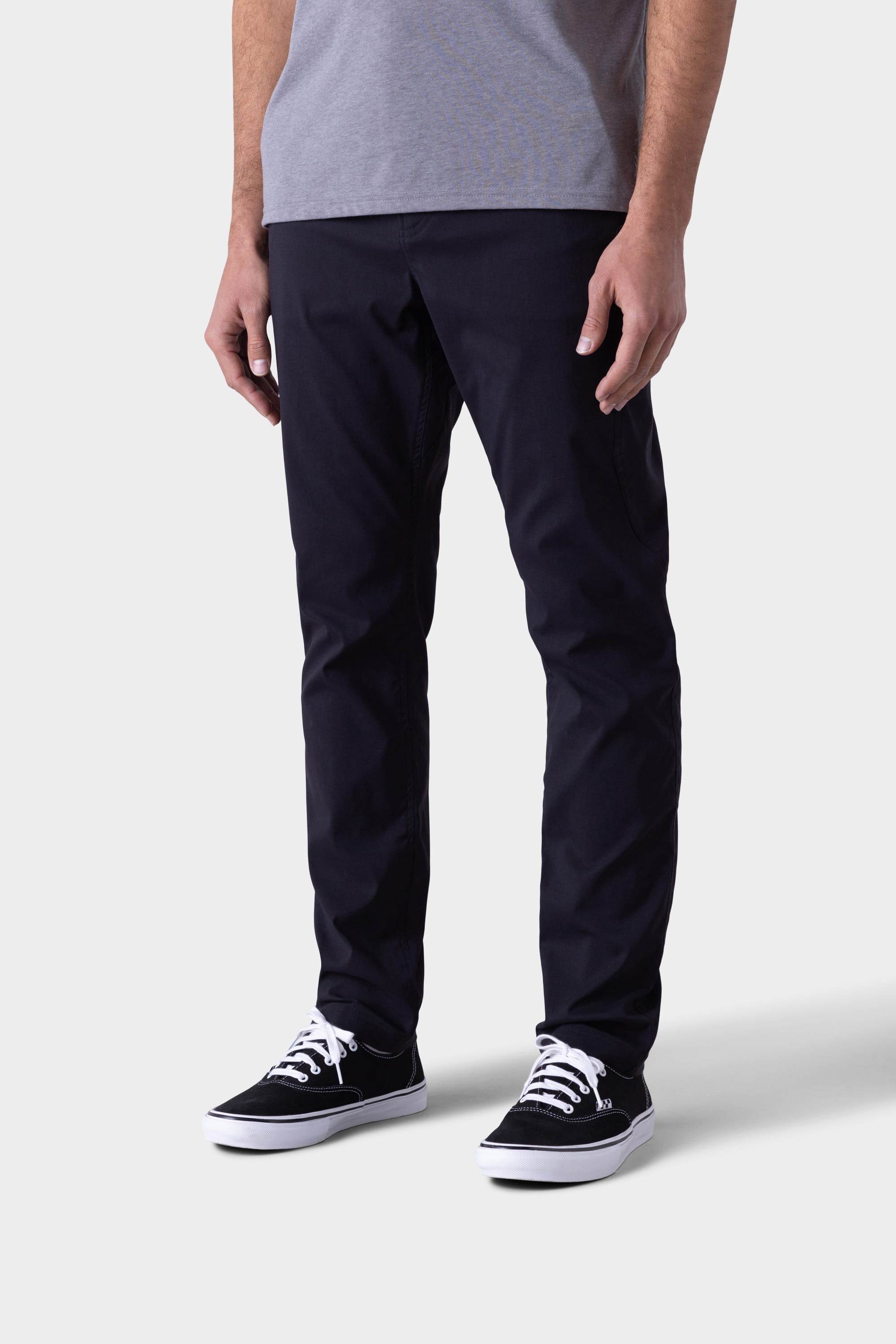 A person is shown from the shoulders down wearing 686 Mens Platform Bike Pant - Slim Fit in black, paired with a grey T-shirt and black-and-white sneakers, standing against a plain light background.