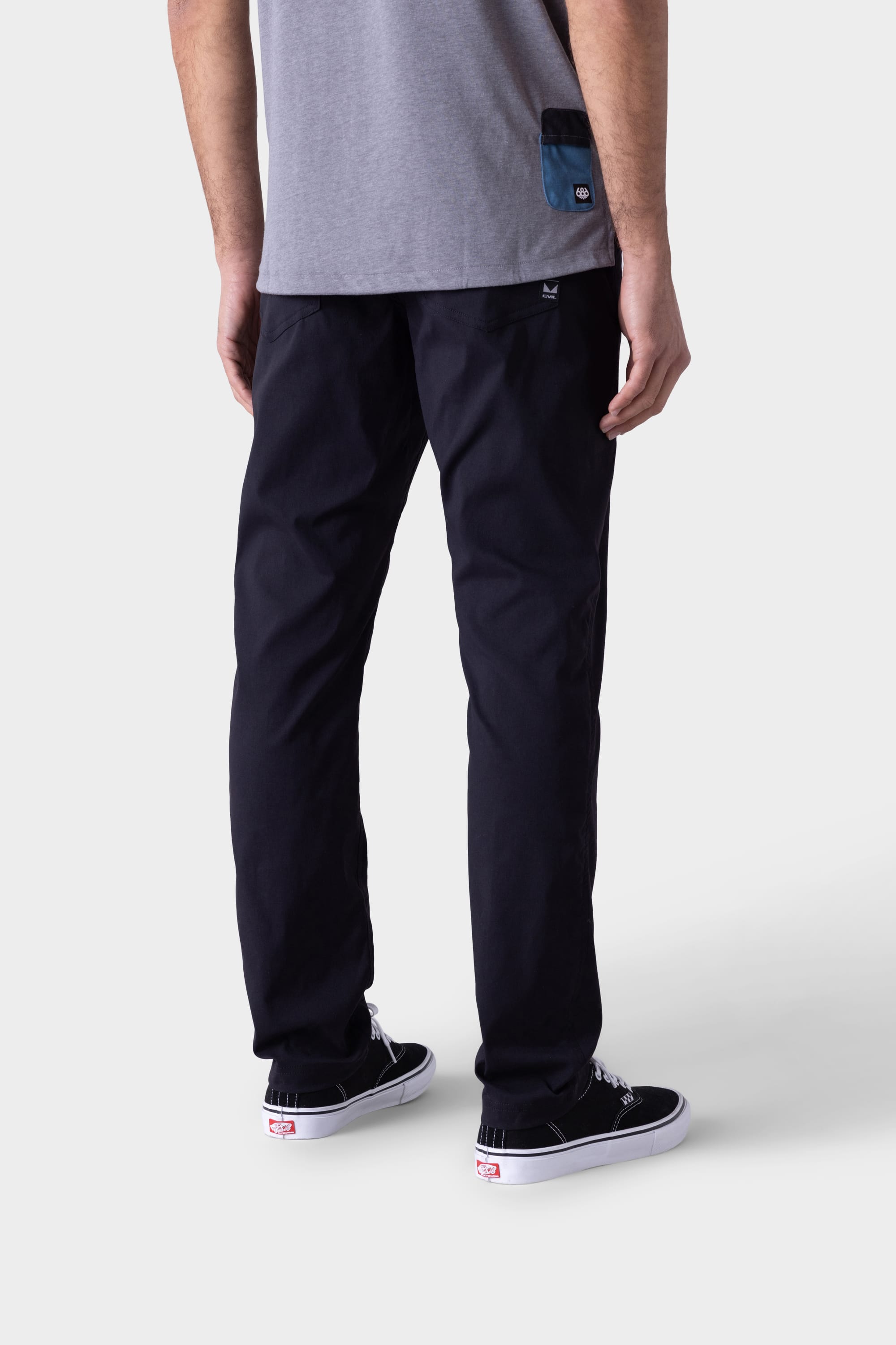 A person stands facing away, wearing a grey t-shirt and the 686 Mens Platform Bike Pant - Slim Fit in black by 686, paired with black sneakers with white soles against a plain light background.