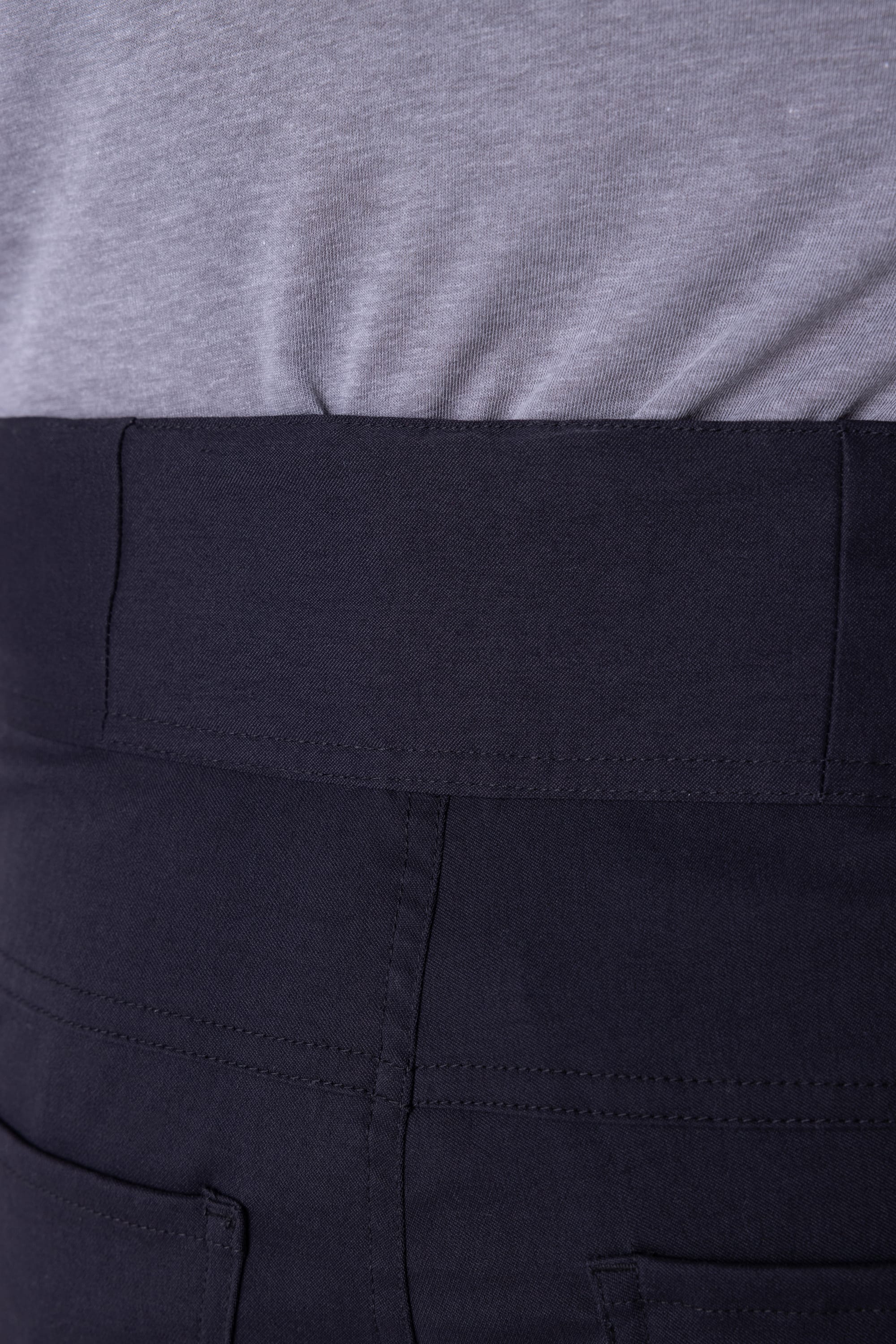 Close-up of a person wearing the 686 Mens Platform Bike Pant - Slim Fit by 686, featuring a high waist, dark fabric, visible stitching, and back pockets paired with a tucked-in light grey shirt.