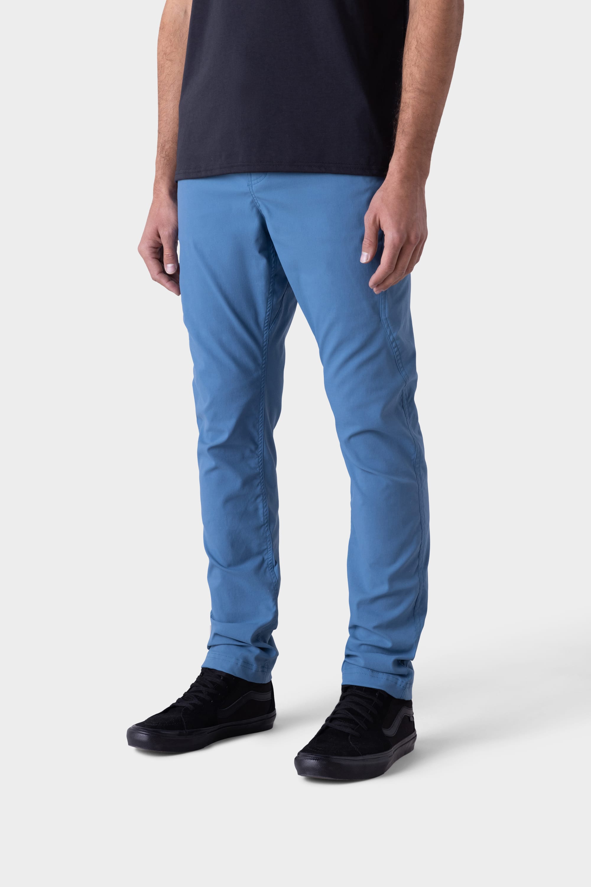 A person models the 686 Mens Platform Bike Pant - Slim Fit in bright blue, paired with a black t-shirt and black sneakers, standing against a plain white background; only their body from the shoulders down is visible.