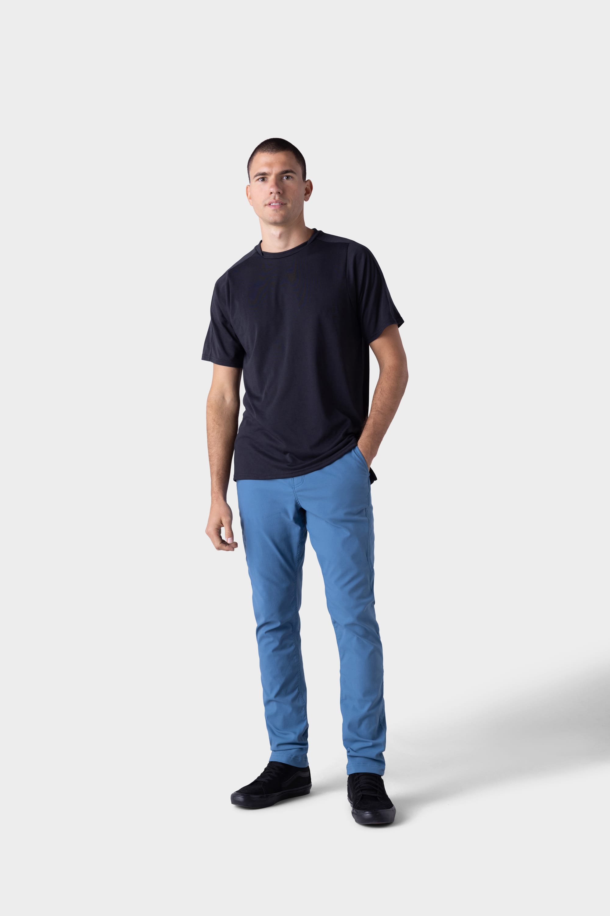 A man wearing the 686 Mens Platform Bike Pant - Slim Fit by 686 stands against a white background, paired with a black t-shirt and black shoes. He faces the camera with a neutral expression, right hand in his pocket.