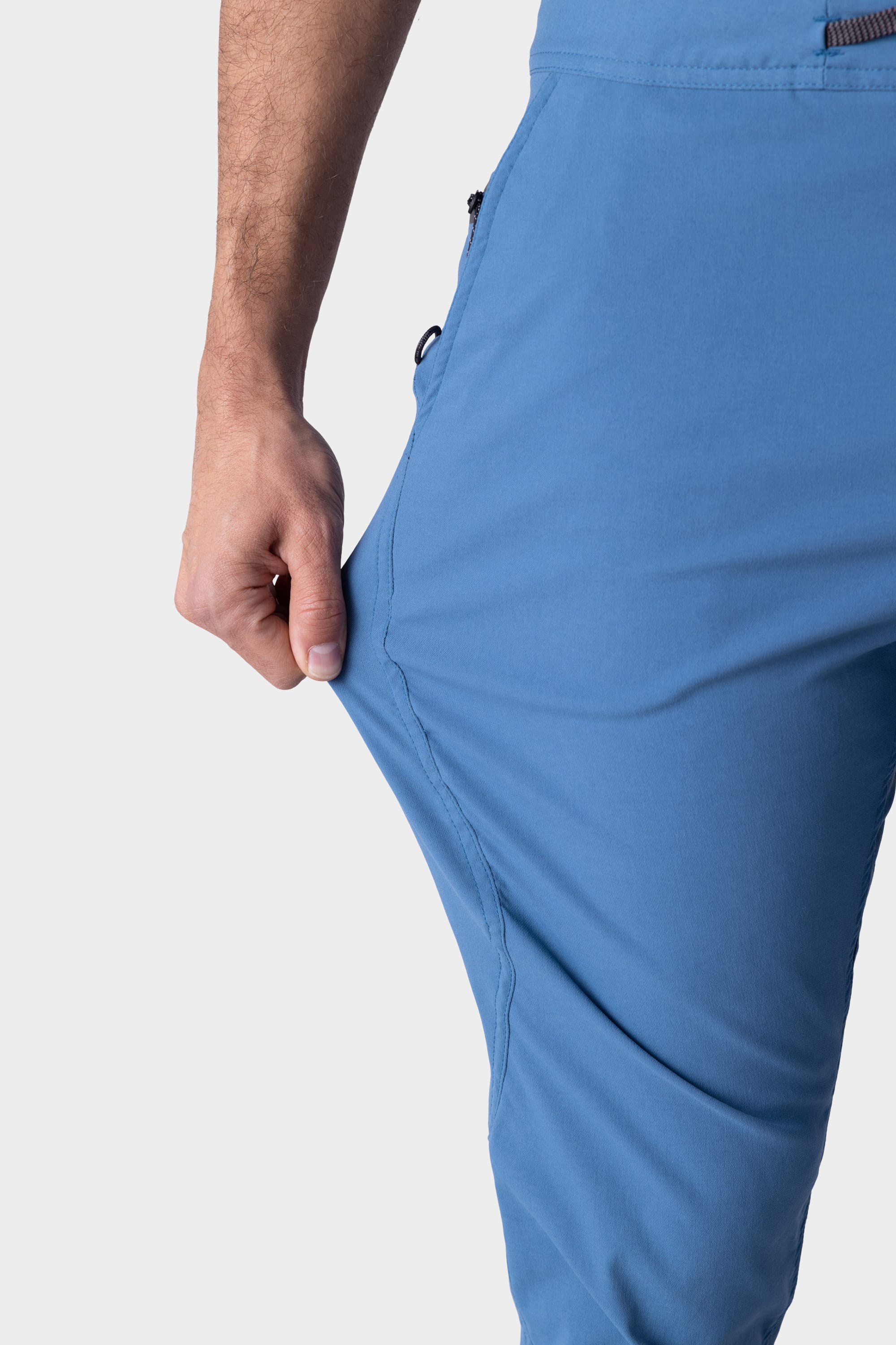 A person stretches the fabric of the 686 Mens Platform Bike Pant - Slim Fit outward with their left hand, highlighting its flexibility. Only the lower torso and one arm are shown against a plain background.